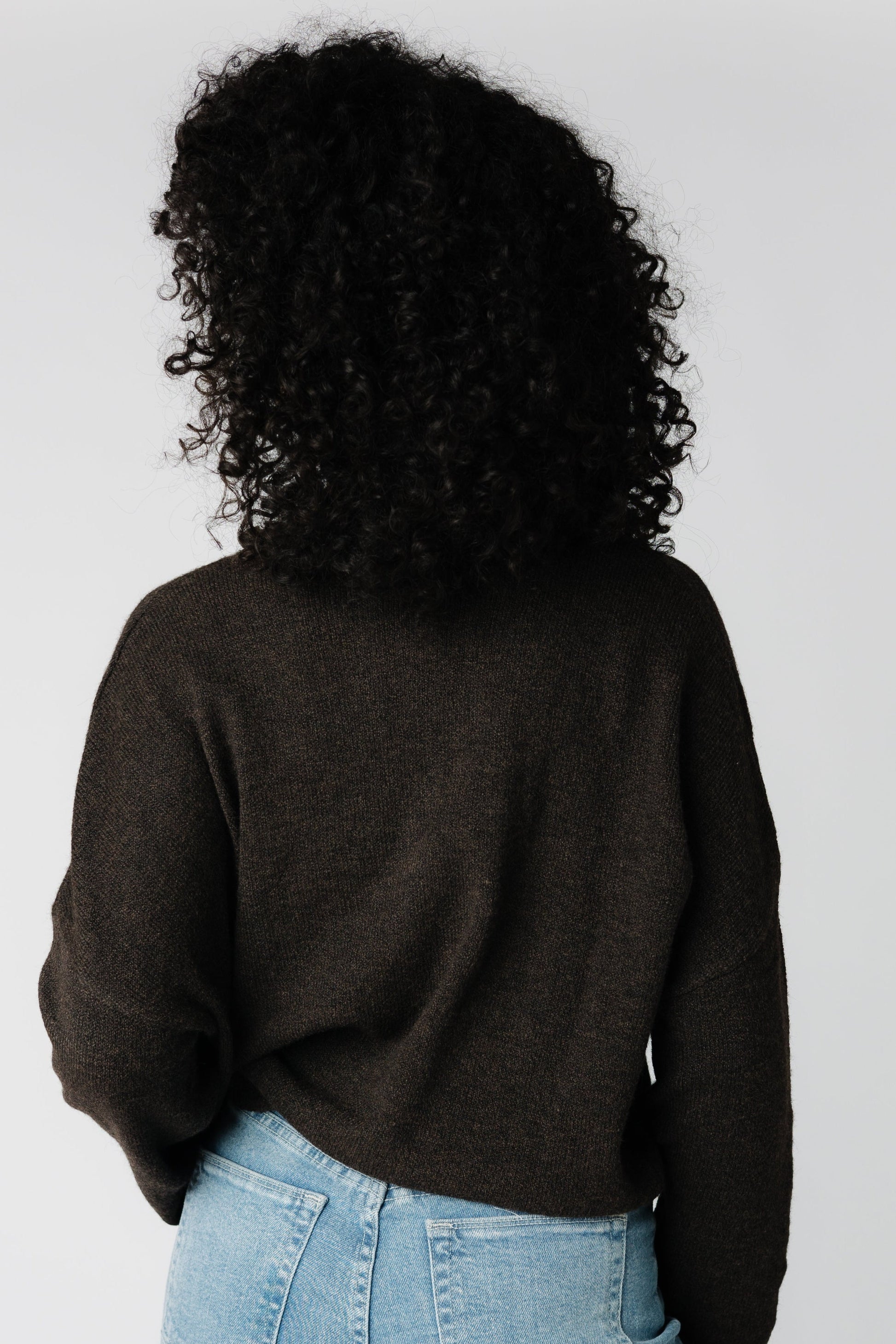 A back view of a woman wearing a brown sweater with long sleeves
