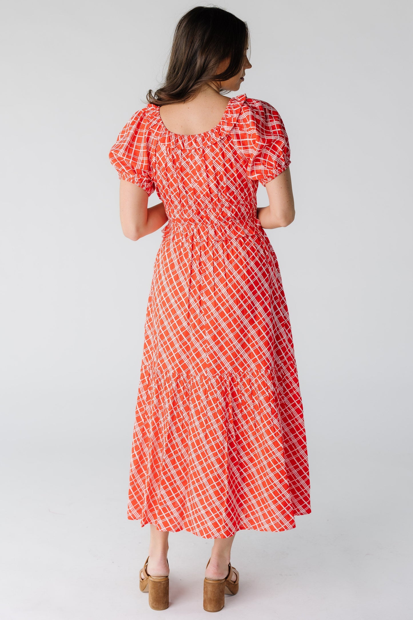 Back view of a woman wearing a red plaid midi dress with a scoop back neckline and short puff sleeves.