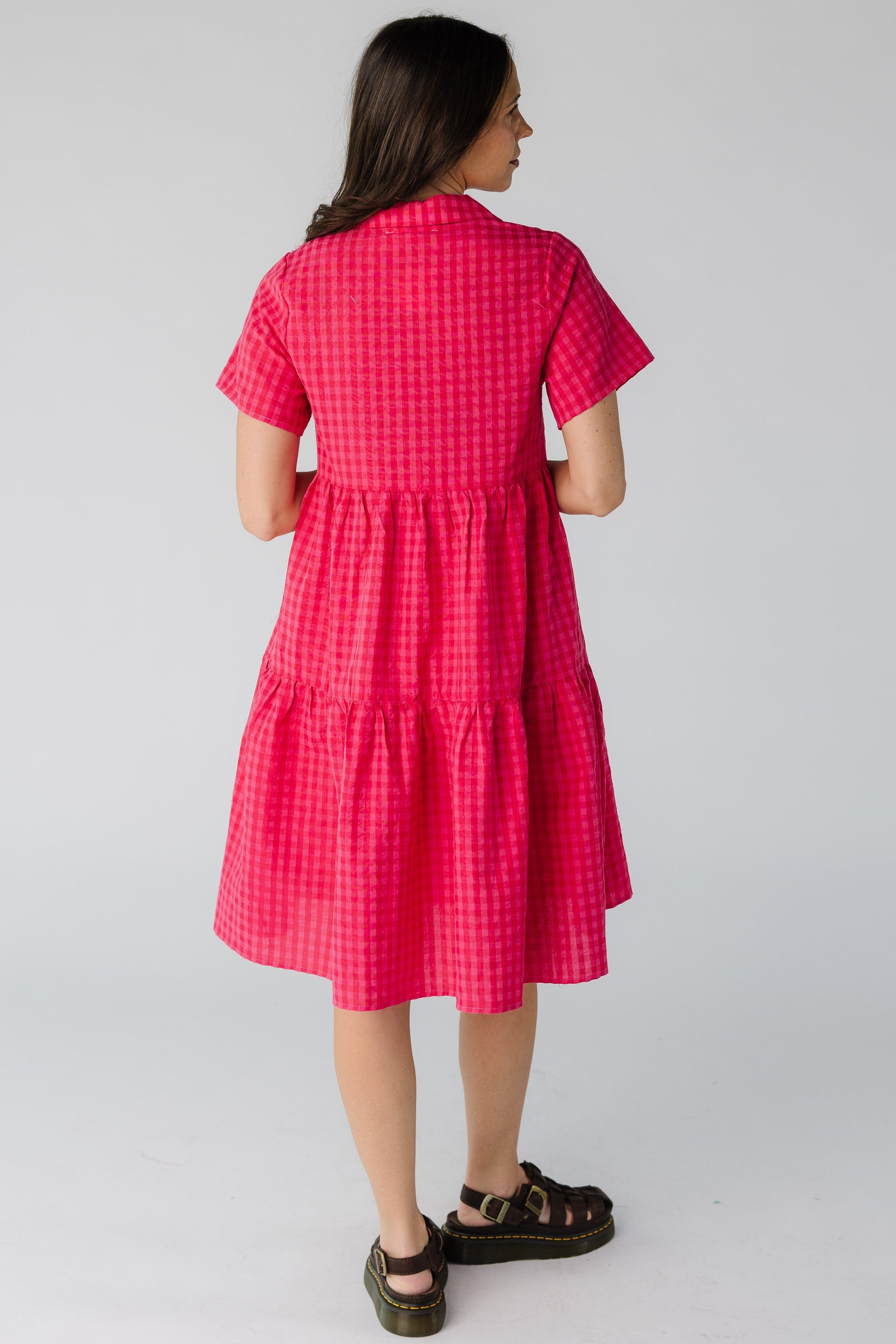 Back view of a woman wearing a red and pink, knee length dress with short sleeves.