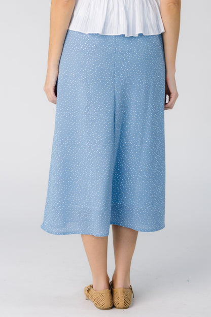 Back view of a woman wearing a light blue midi skirt with small white polka dots.