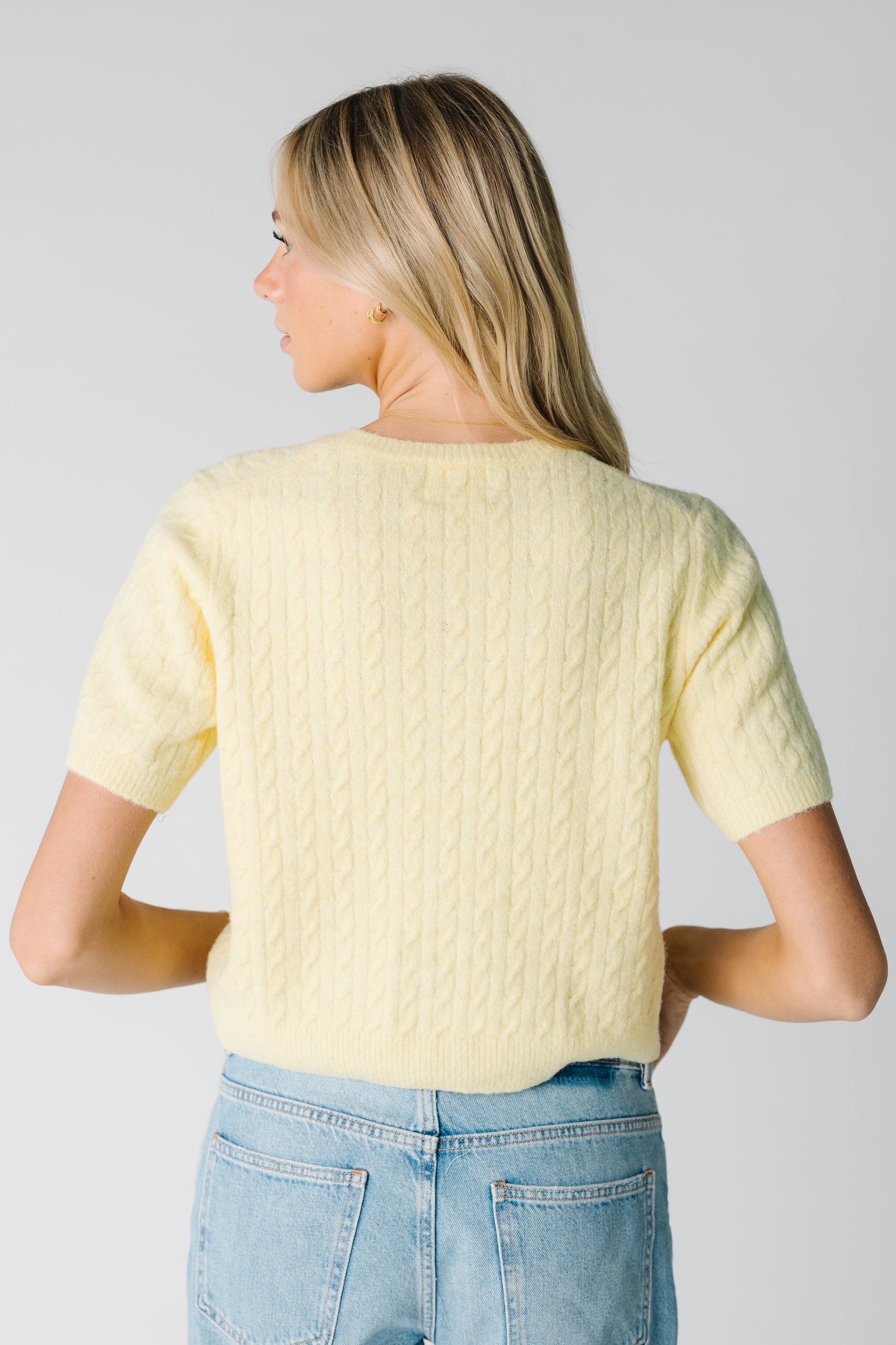 Back view of pale yellow cable knit cardigan with short sleeves