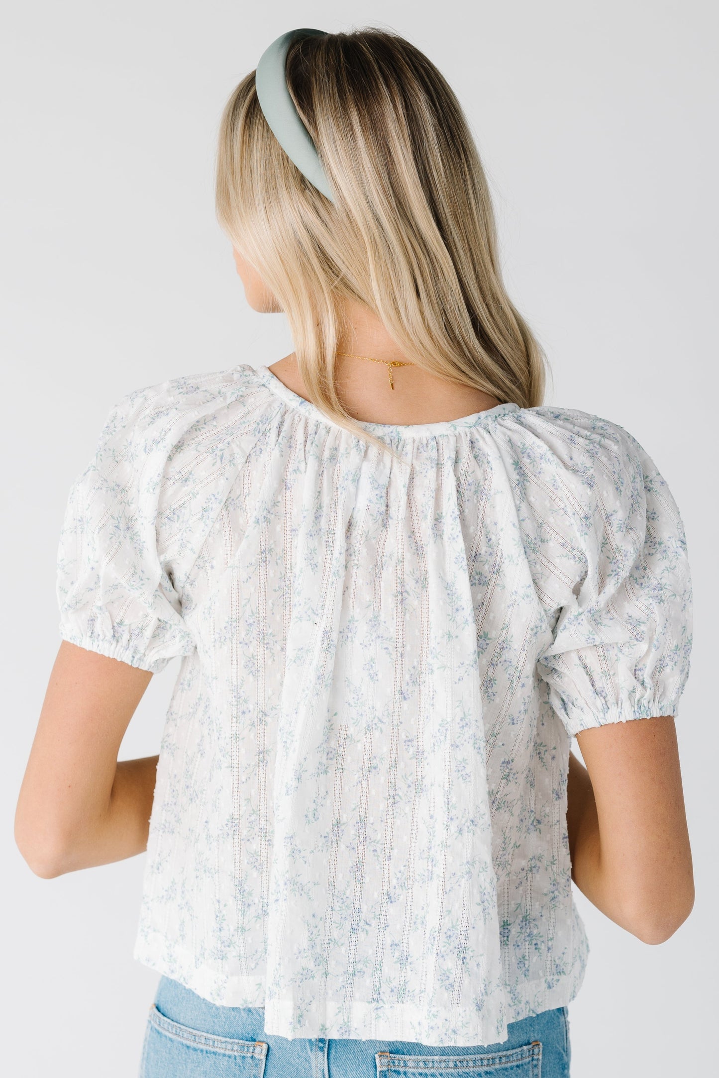 Back view of white lightweight  top with blue floral pattern and short sleeves