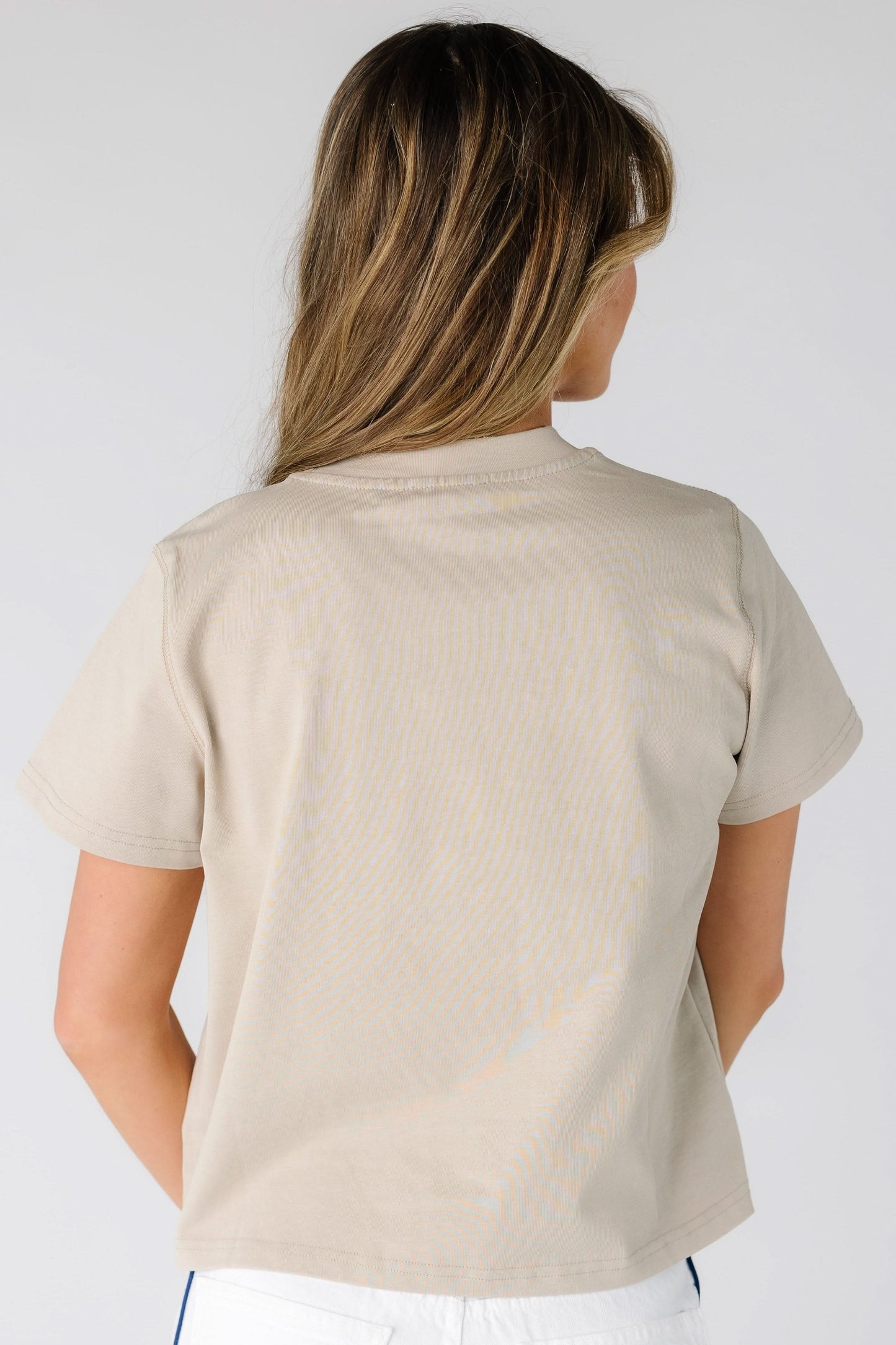 Back view of a young woman wearing a beige short sleeve tee.