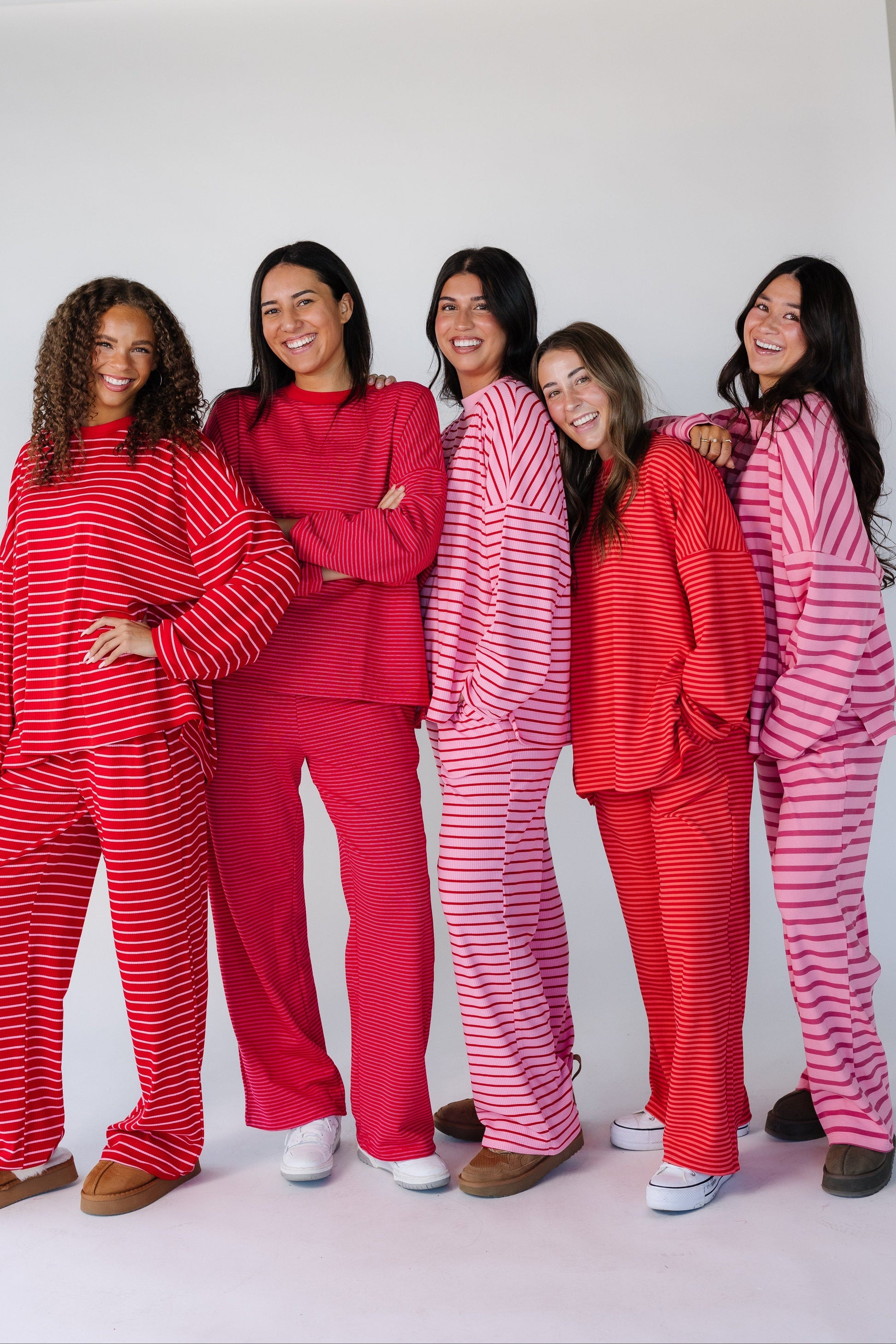 5 women wearing pink and red stripe loose fitting lounge sets with long sleeves and long pants.