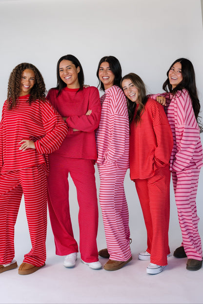 5 women wearing pink and red stripe loose fitting lounge sets with long sleeves and long pants.
