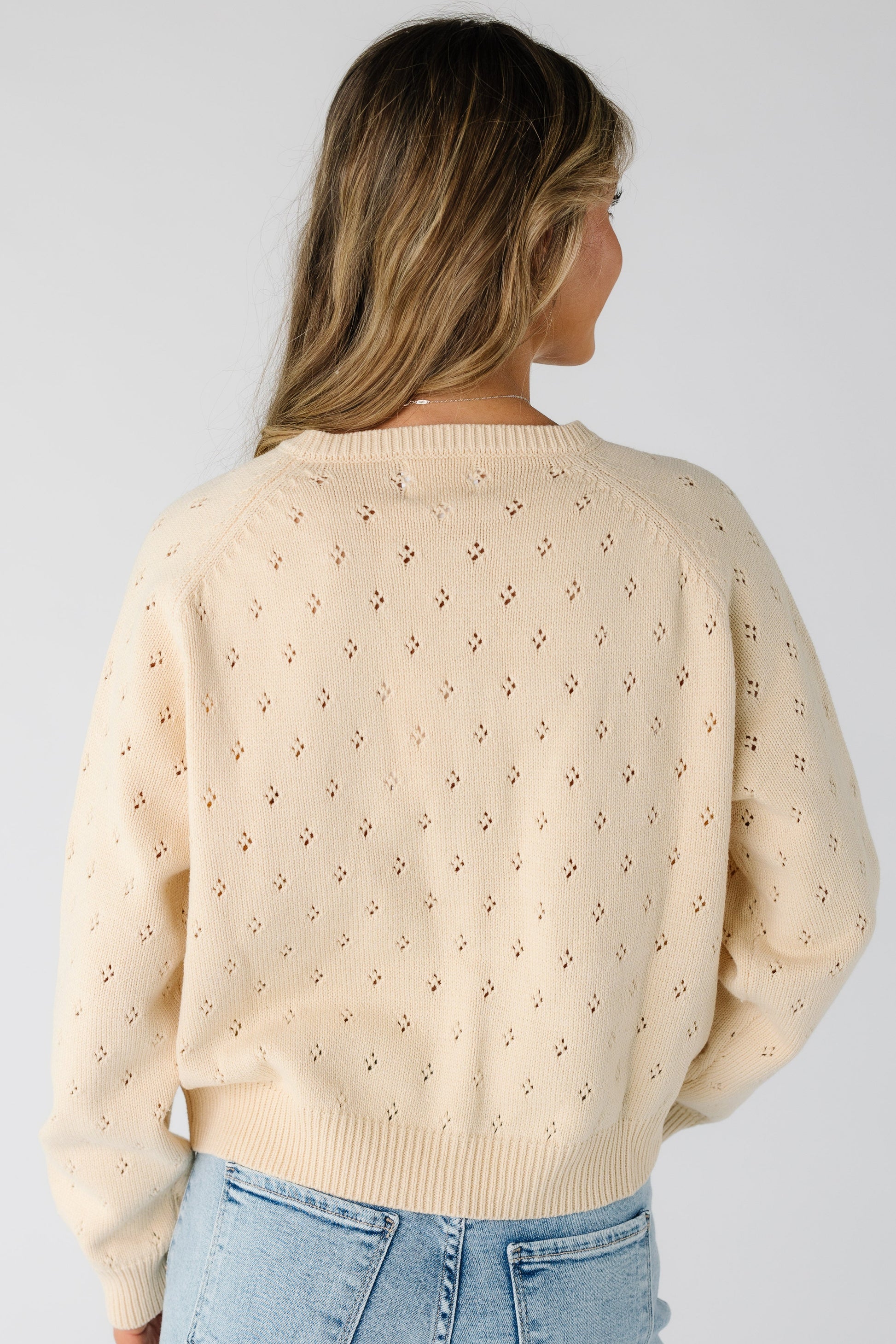 Back view of a woman wearing a  cream eyelet knit cardigan with long sleeves.