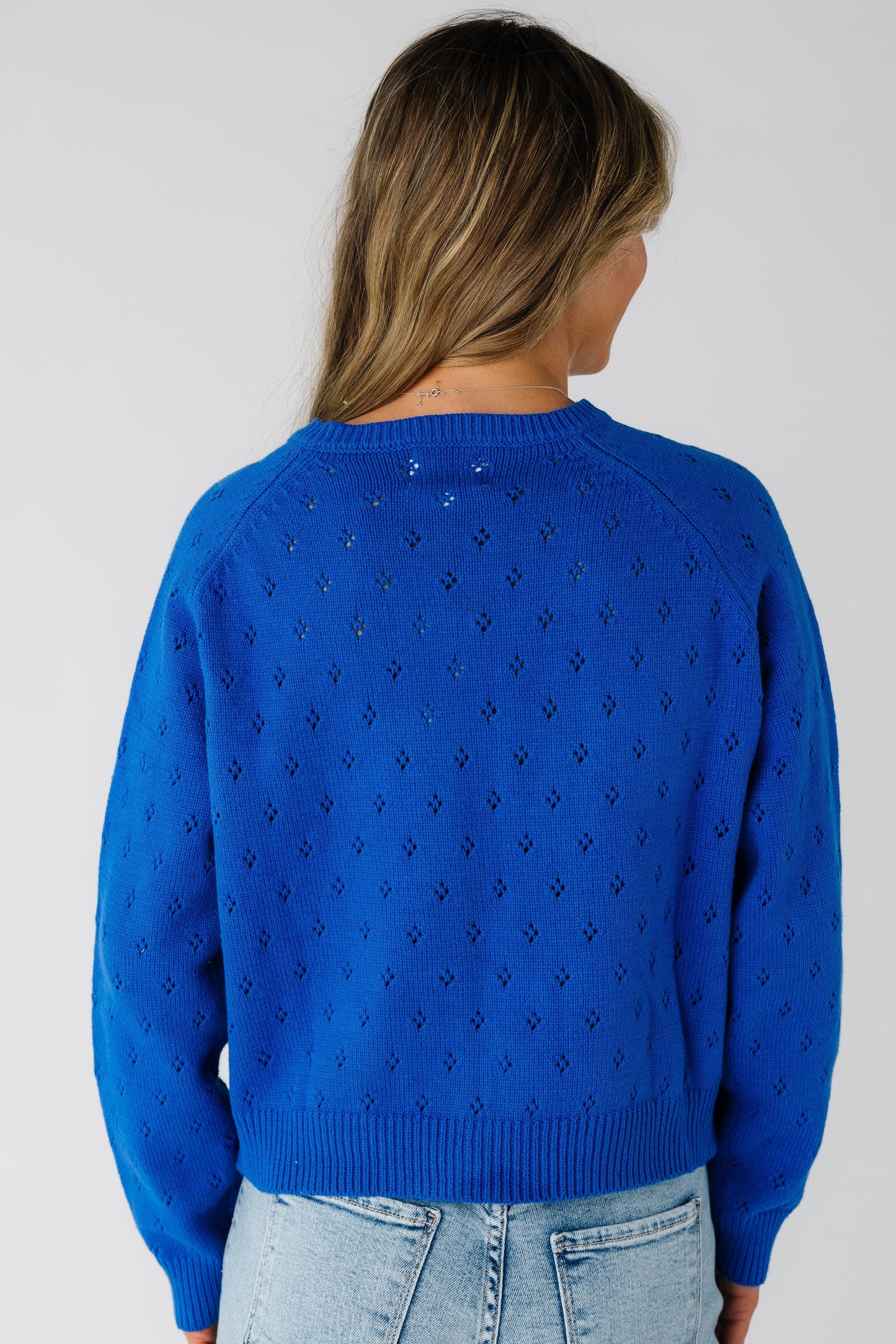 Back view of a woman wearing a royal blue cardigan in an eyelet knit.