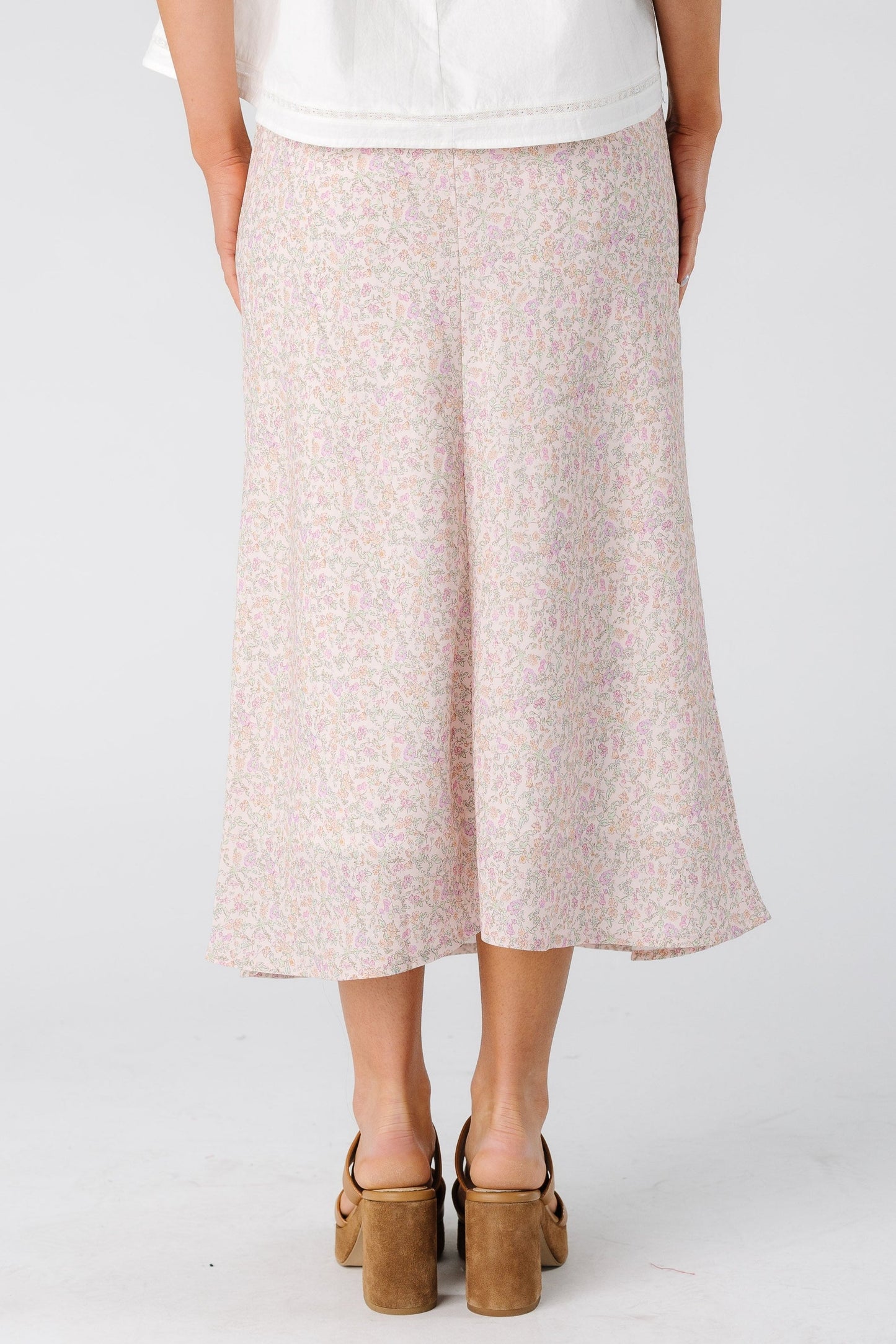 Back view of a woman wearing a light pink floral skirt in midi length.