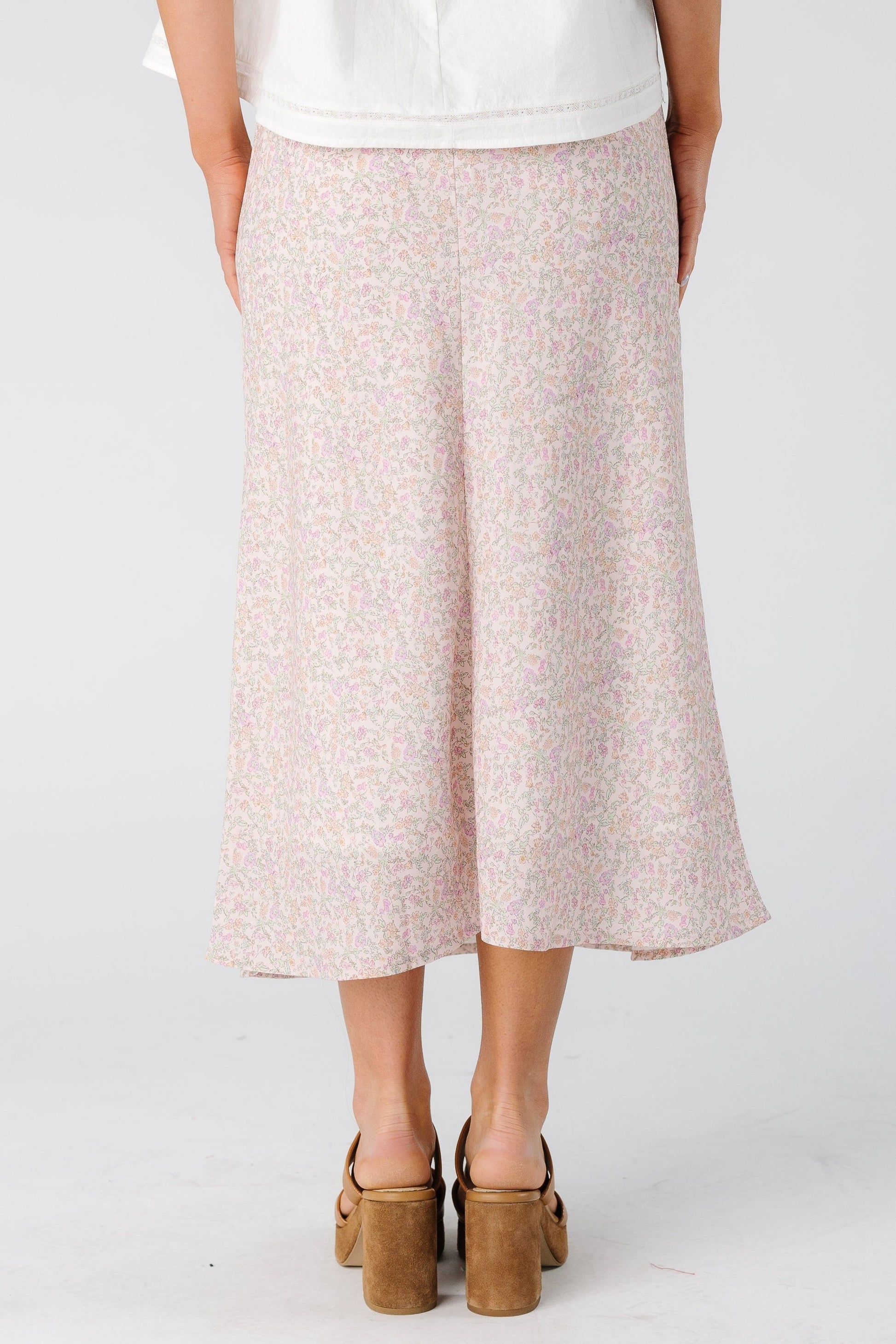 Back view of a woman wearing a light pink floral skirt in midi length.