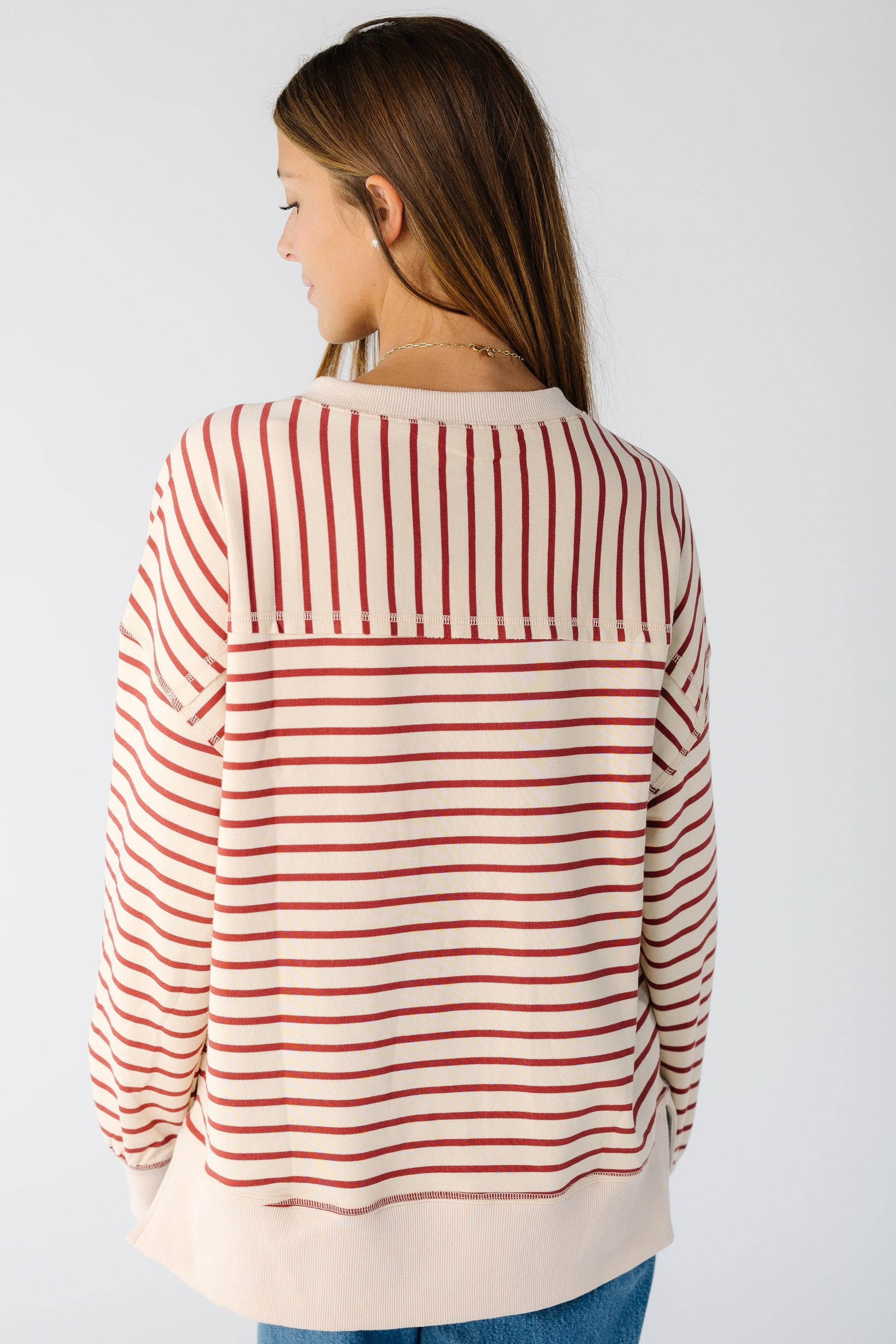 Back view of a woman wearing a beige and brick stripe loose fitting top with long sleeves