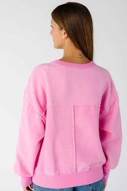 Back view of a woman wearing a pink long sleeve reversible sweatshirt