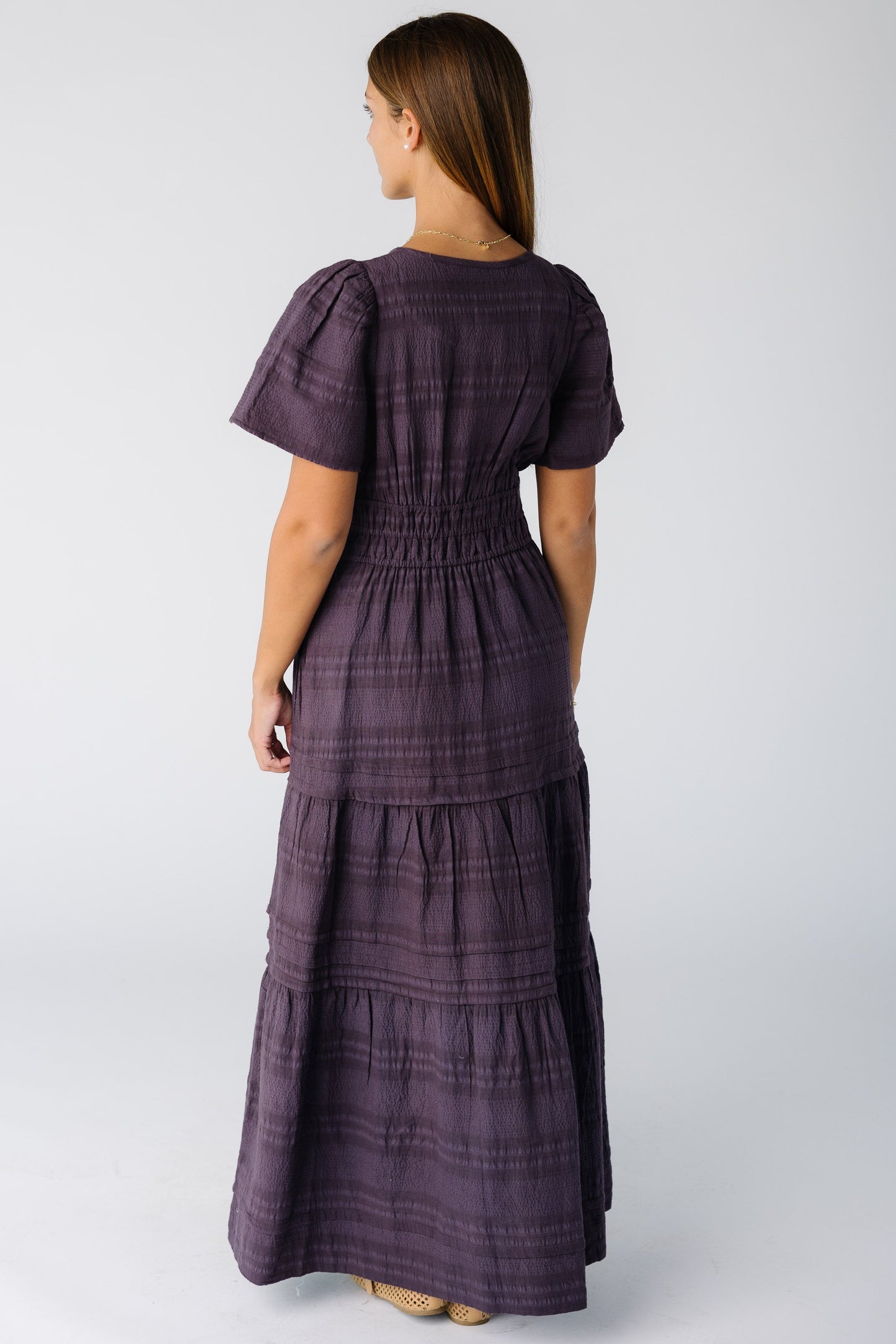 Back view of a woman wearing a plum textured stripe maxi dress with a wide snug waistband