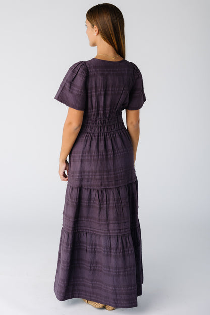 Back view of a woman wearing a plum textured stripe maxi dress with a wide snug waistband