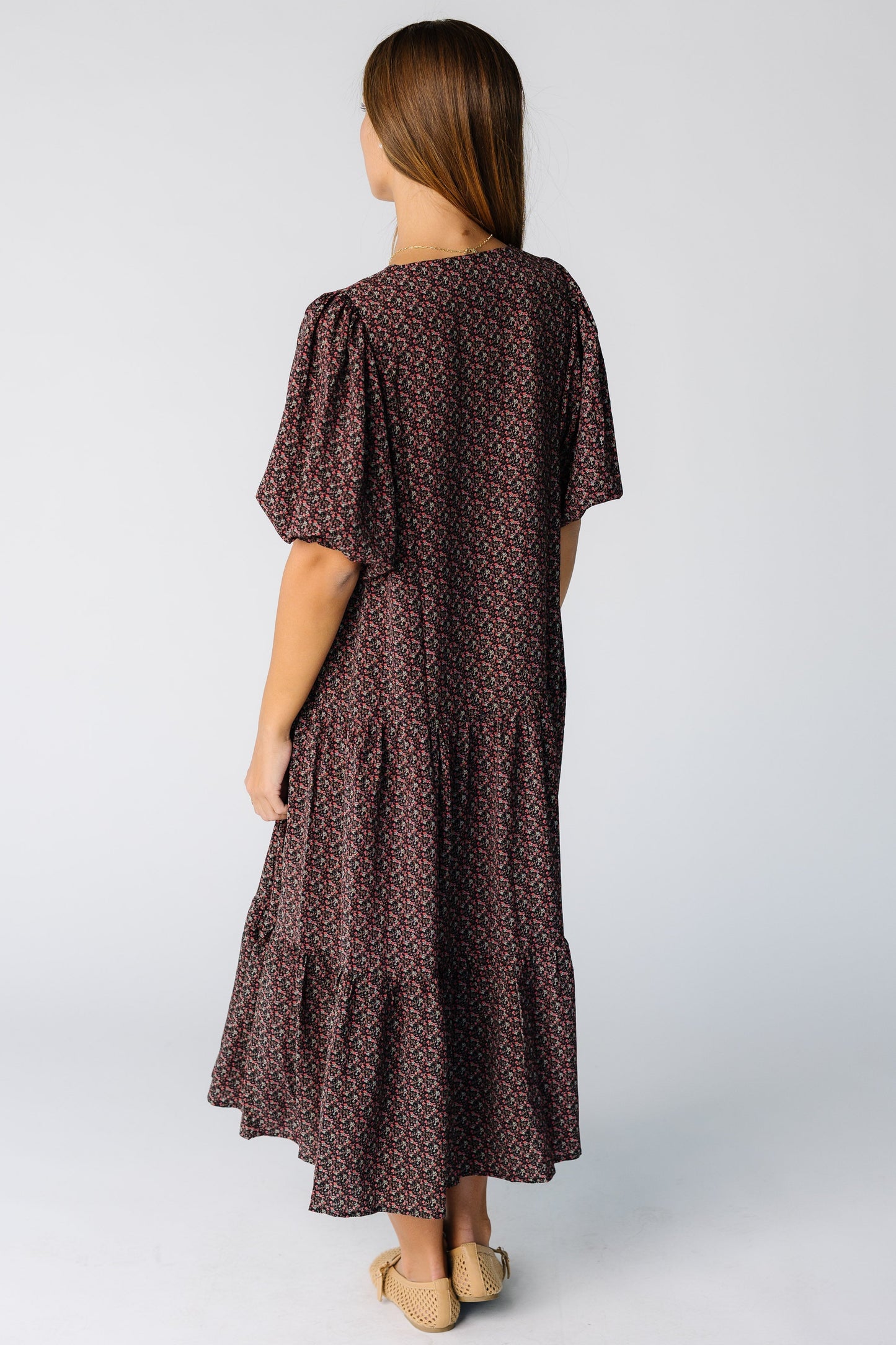 Back view of a woman wearing a black floral print midi dress with elbow length sleeves