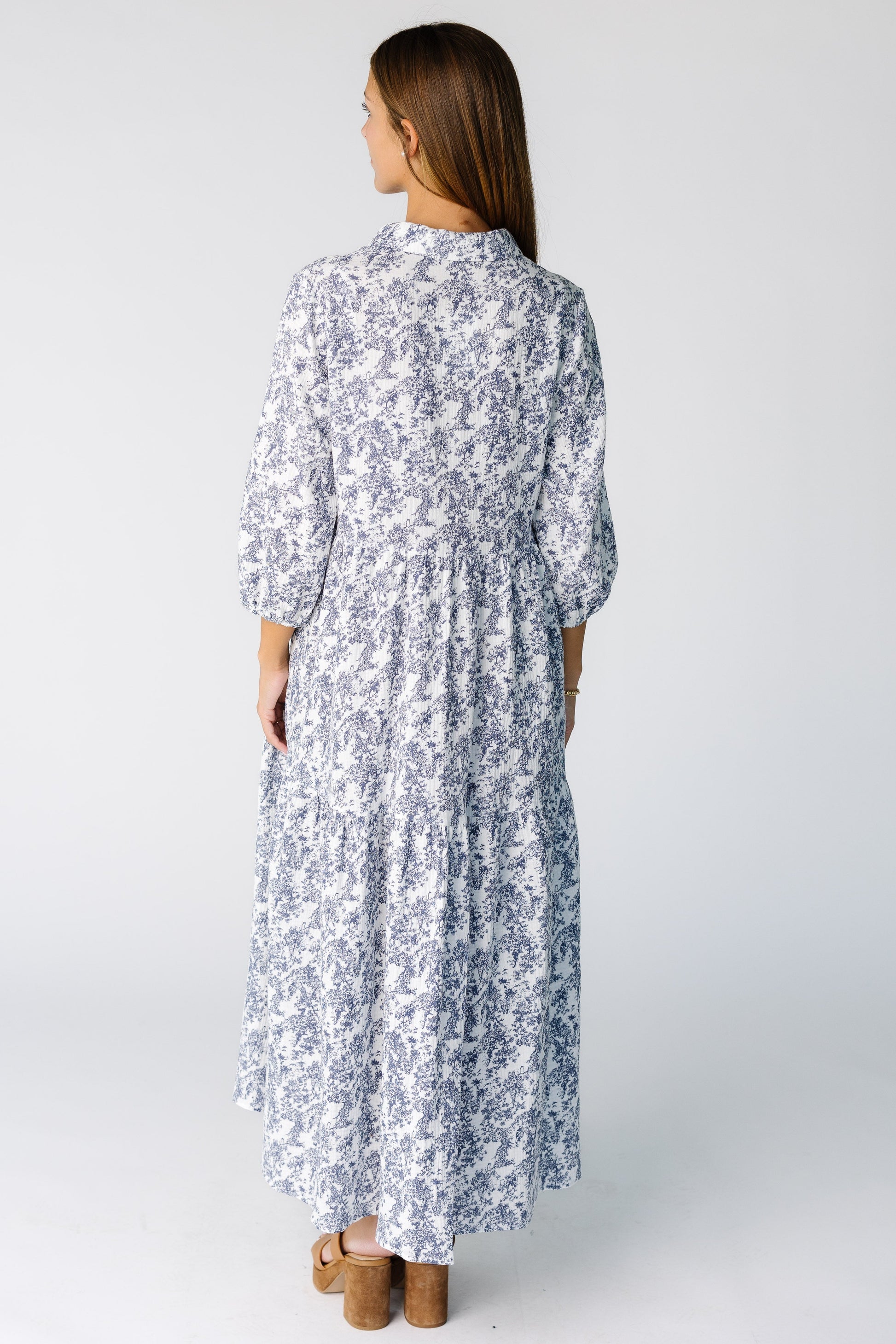 Back view of a woman wearing a white and blue print midi dress with 3/4 length sleeves