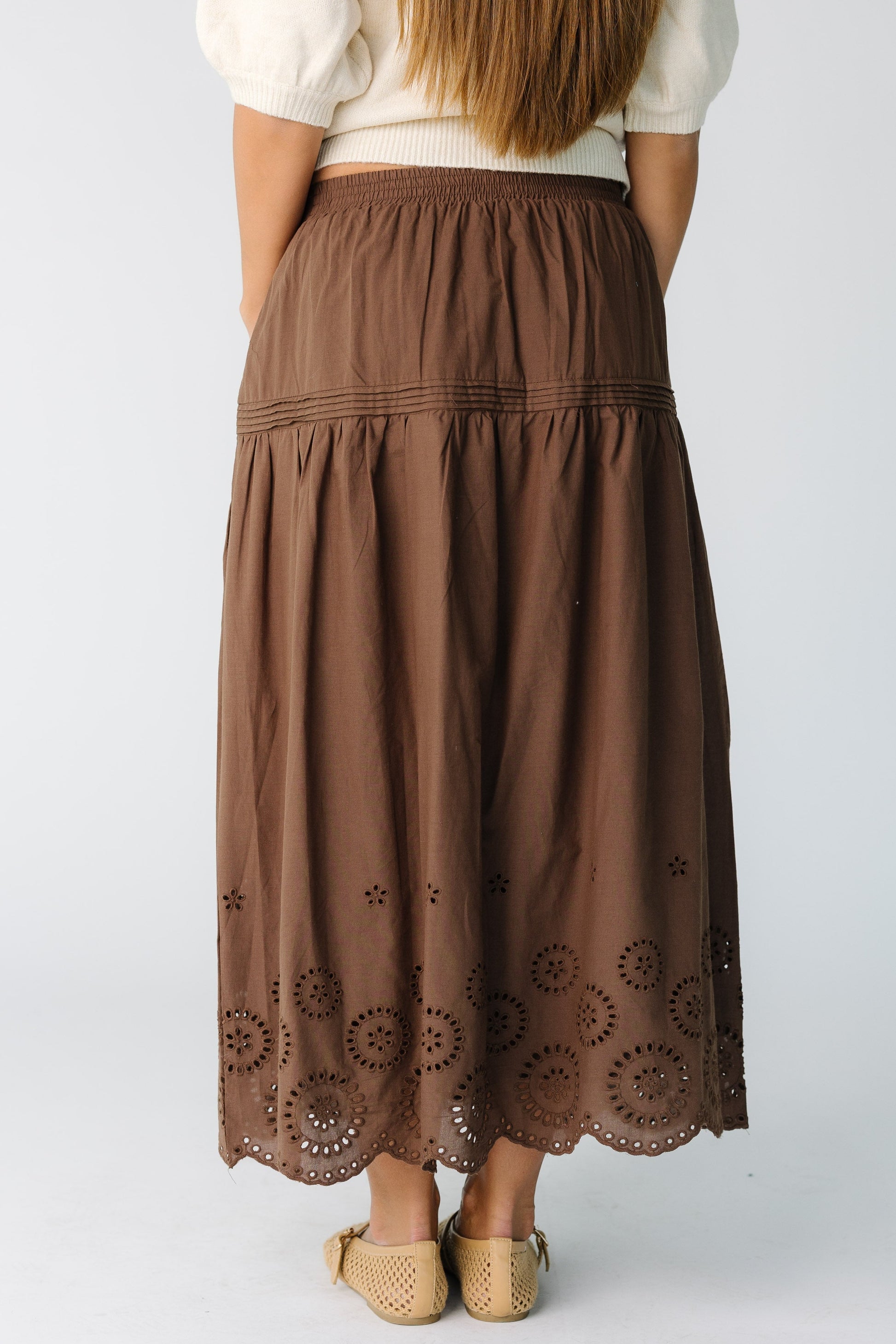 Back view of a woman wearing a brown mdi skirt with eyelet hemline