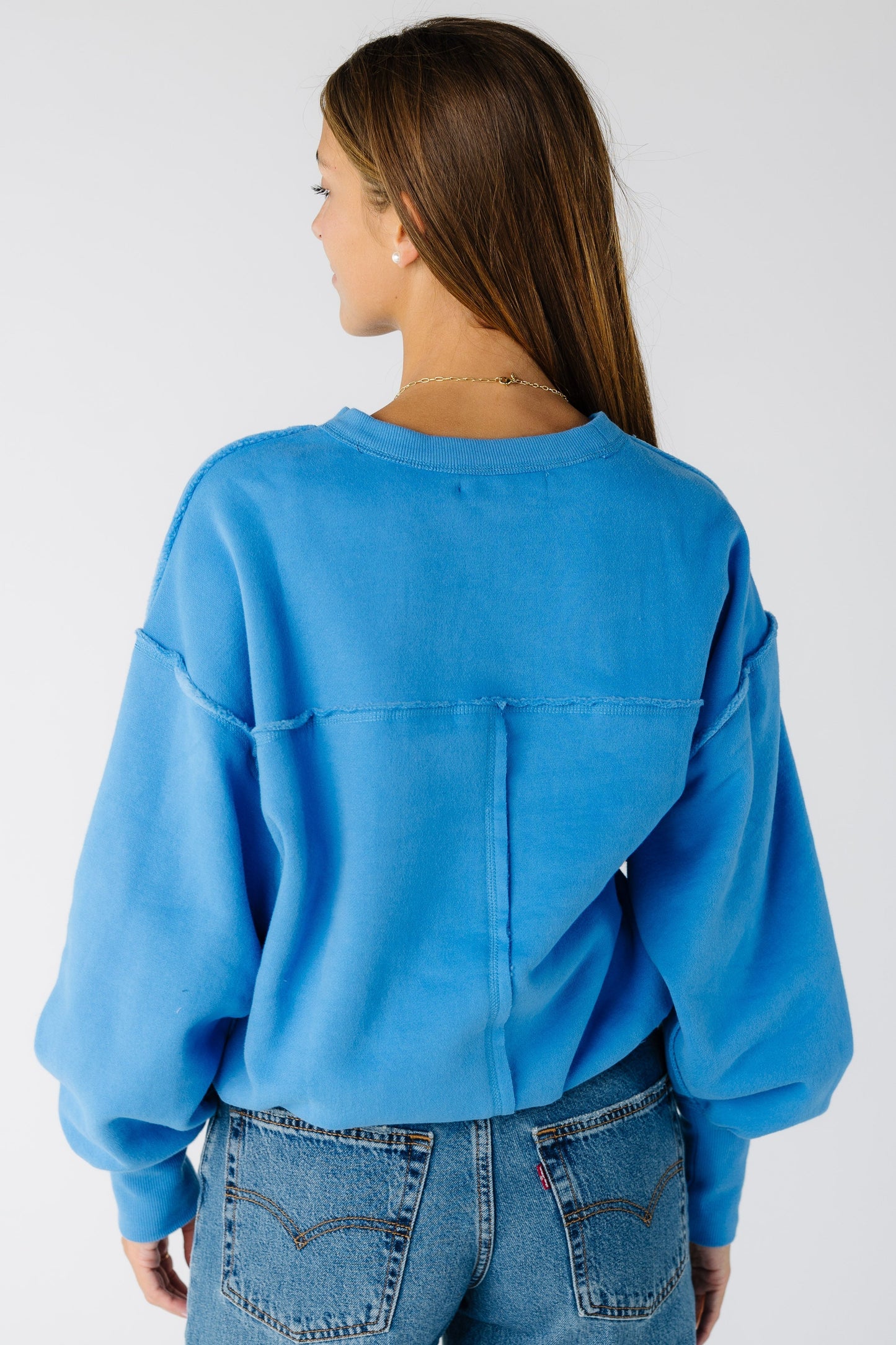 Back view of a woman wearing al blue sweatshirt with exposed seams