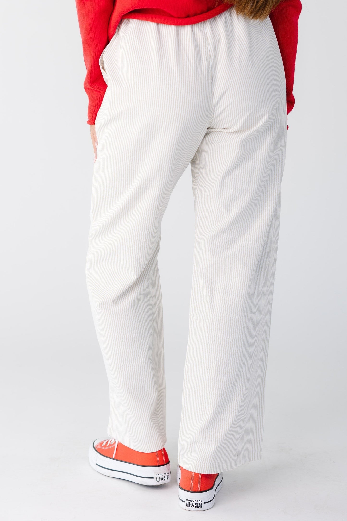 Back view of a woman wearing a pair of taupe and white stripe pants with a wide cut leg