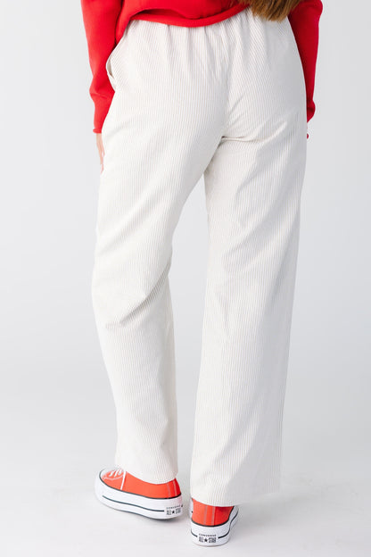 Back view of a woman wearing a pair of taupe and white stripe pants with a wide cut leg