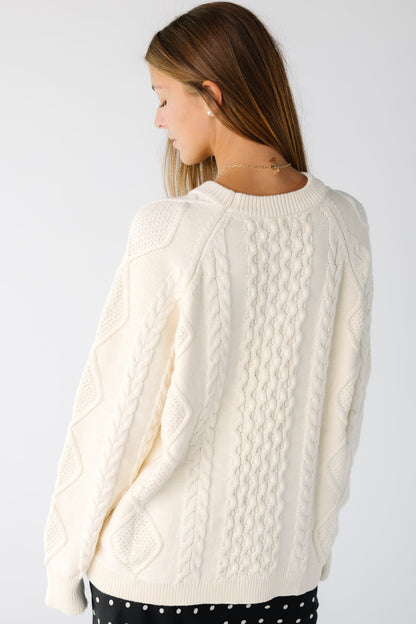 Back view of a woman wearing a white cable knit sweater with long sleeves