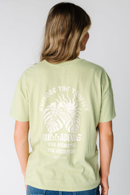 Back view of a woman wearing  a light green graphic tee by Billabong with short sleeves.  24B352507