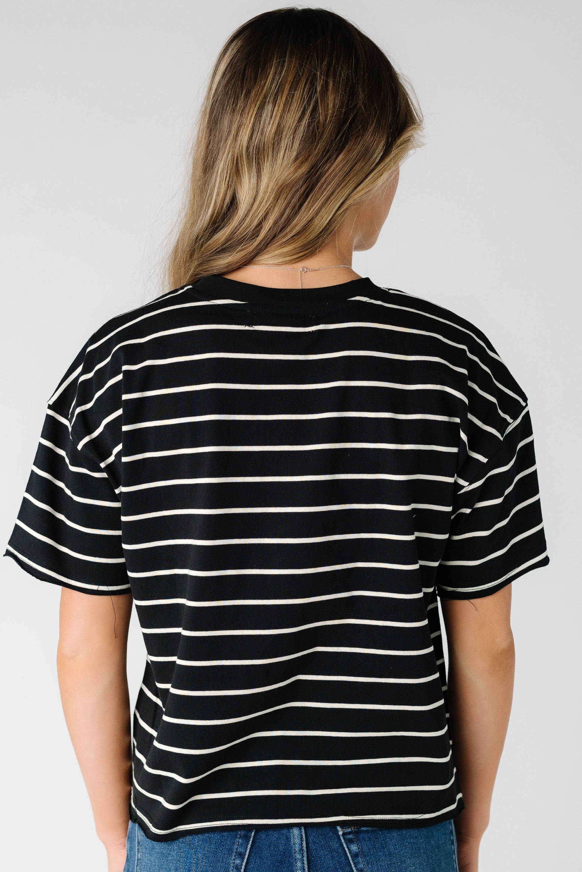 Back view of a woman wearing a black short sleeve tee with white stripes.