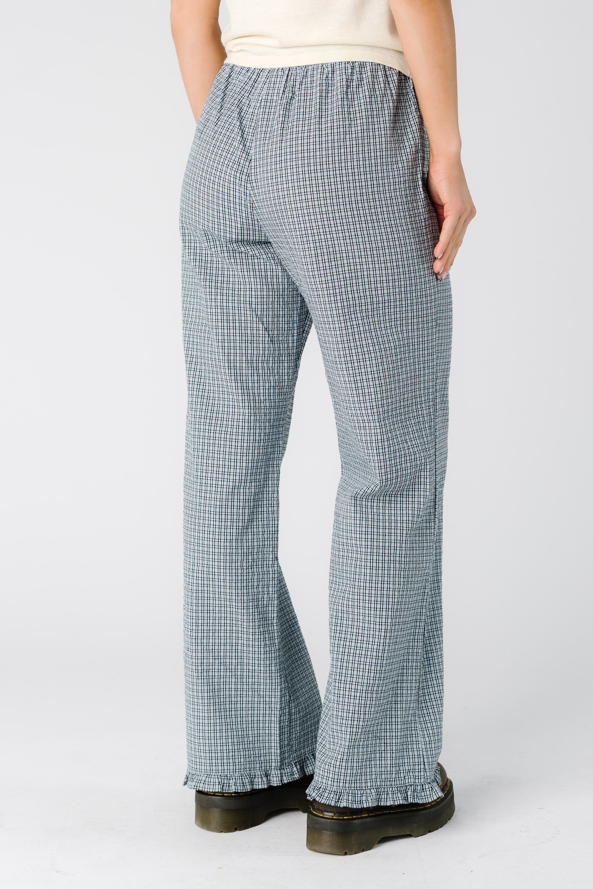 Back view of a woman wearing a pair of blue plaid pants with a ruffle hem