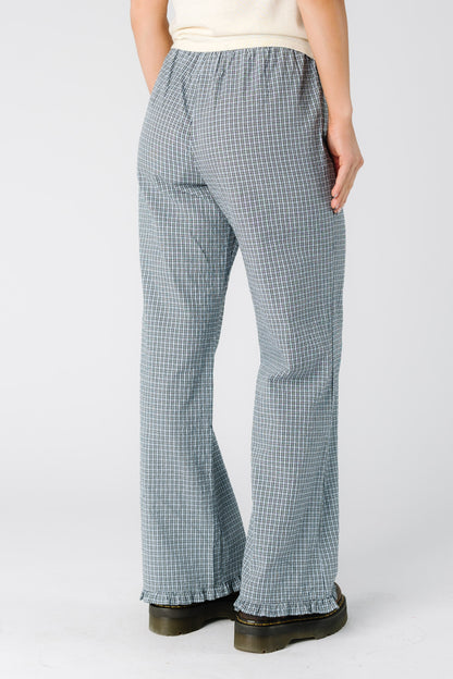 Back view of a woman wearing a pair of blue plaid pants with a ruffle hem