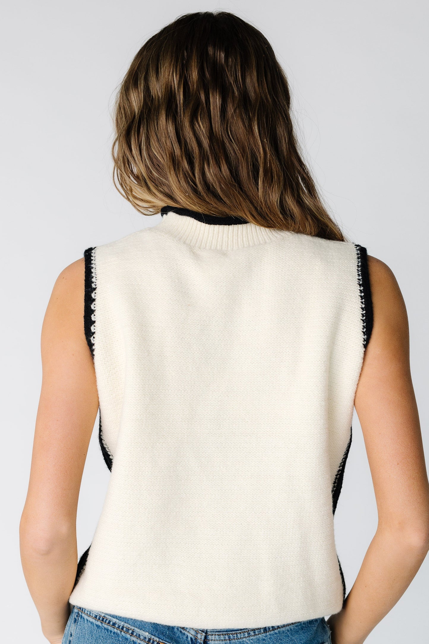 Back view of a woman wearing a cream sleeveless sweater with black trim