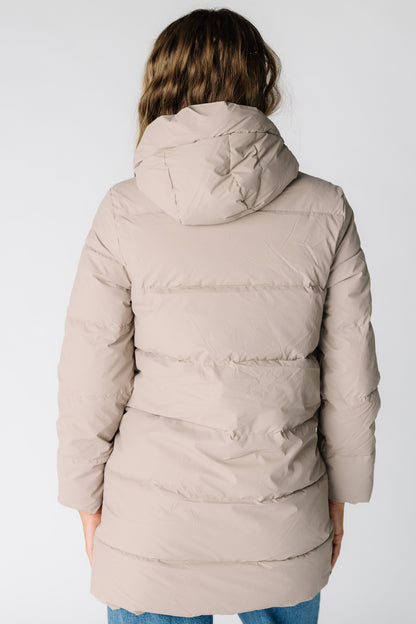 Back view of a woman wearing a taupe puffer jacket with long sleeves and a puffy hood