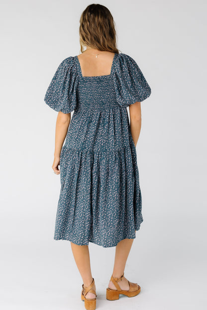 Back view of a woman wearing a blue floral dress with smocked back bodice and a full midi skirt