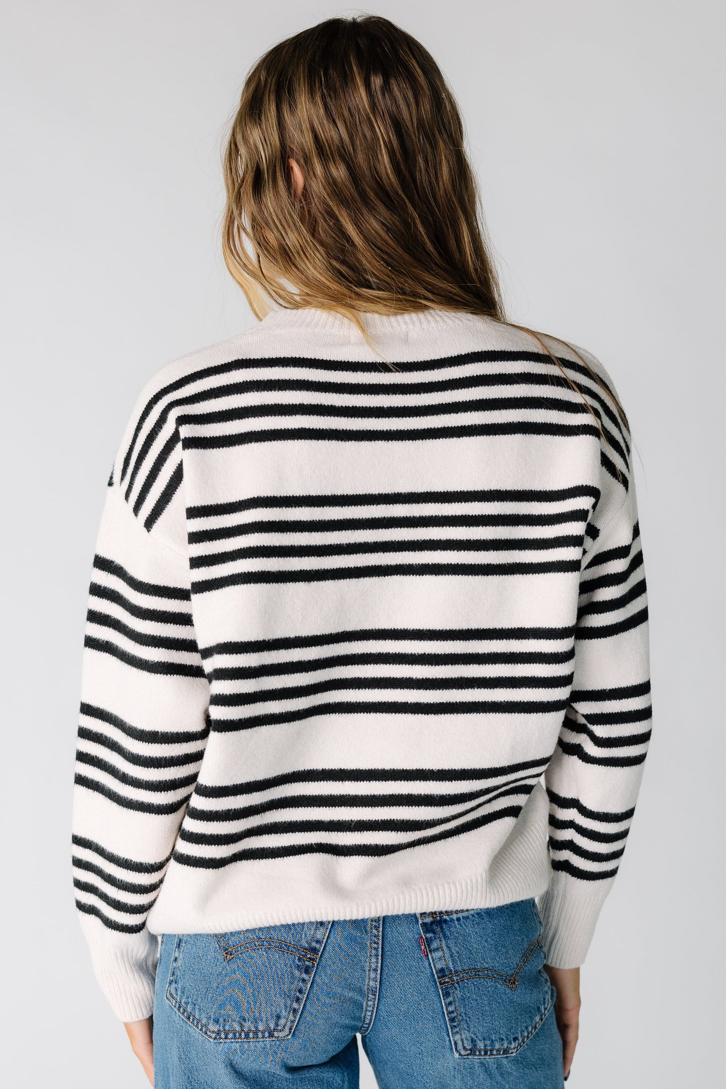 Back view of a woman wearing a light beige sweater with black stripes and long sleeves