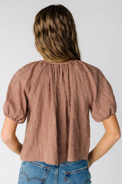 Back view of a woman wearing a loose fitting  taupe gingham top with short puff sleeves