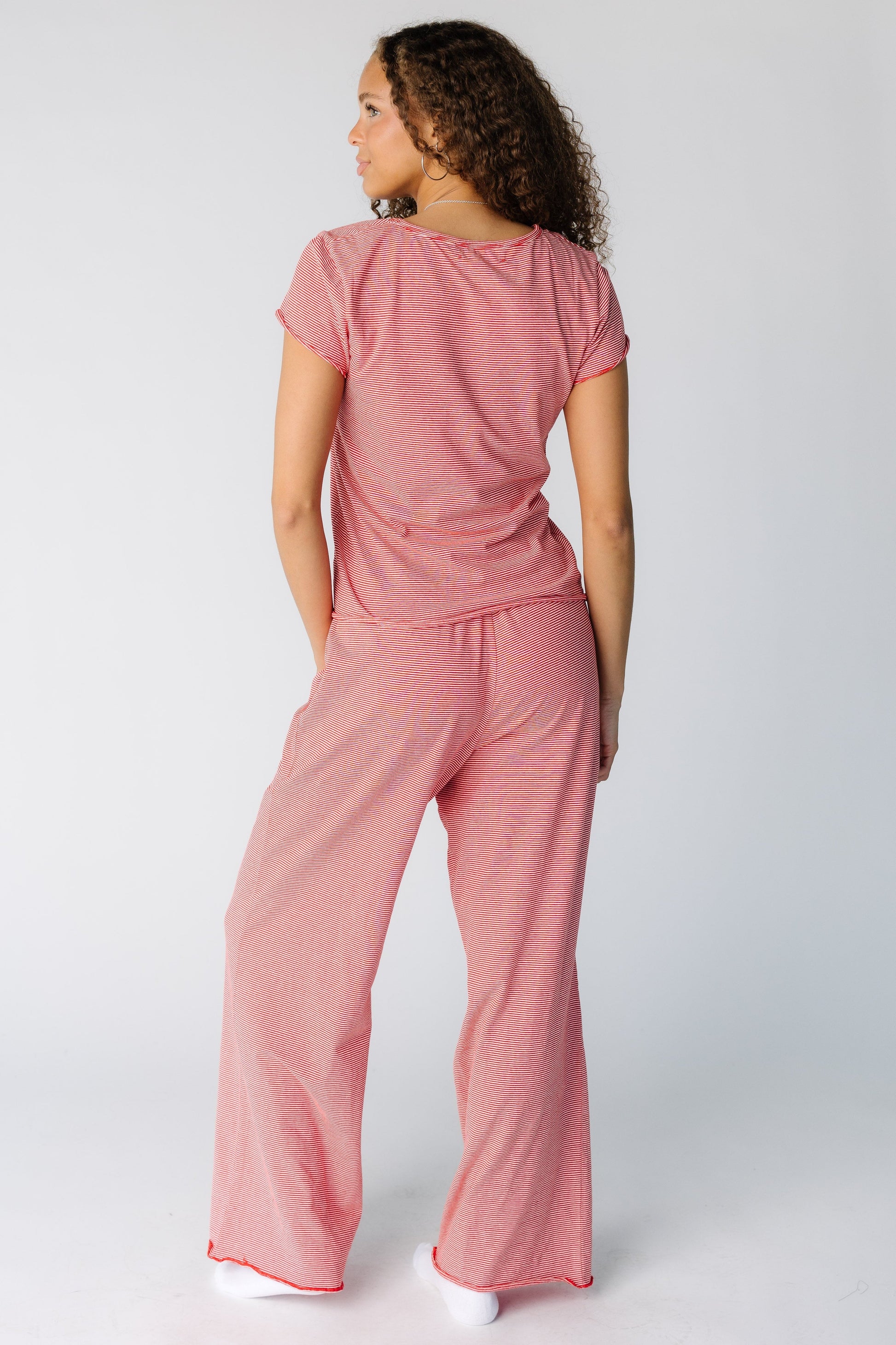 Back view of a woman wearing a red stripe pajama top and bottom with long wide cut pajama bottoms