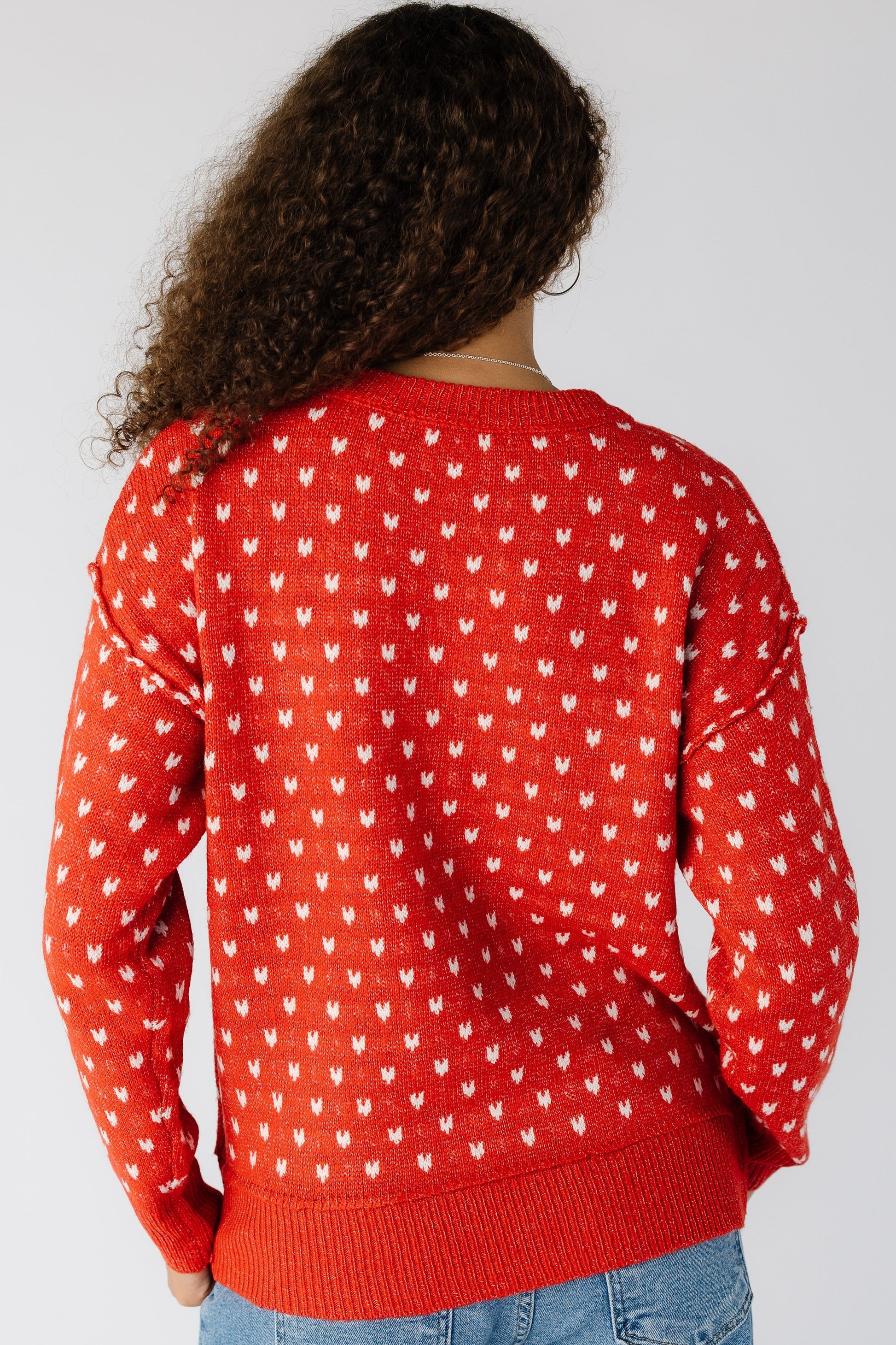 Back view of a woman wearing a red pullover with white knit hearts with wide ribbing