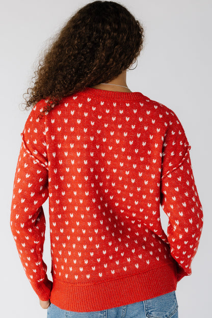 Back view of a woman wearing a red pullover with white knit hearts with wide ribbing