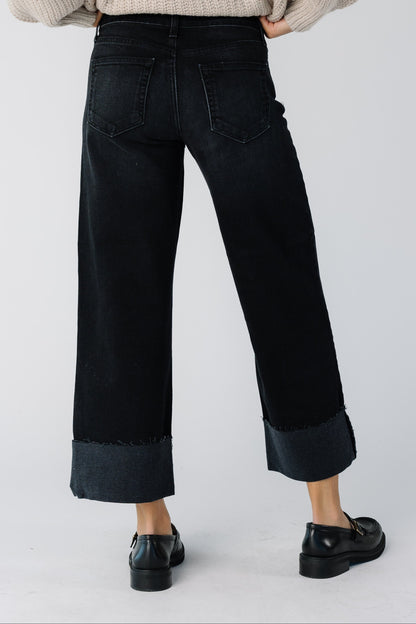 Back view of a teen girl wearing a pair of wide cut black jeans with a wide bottom cuff