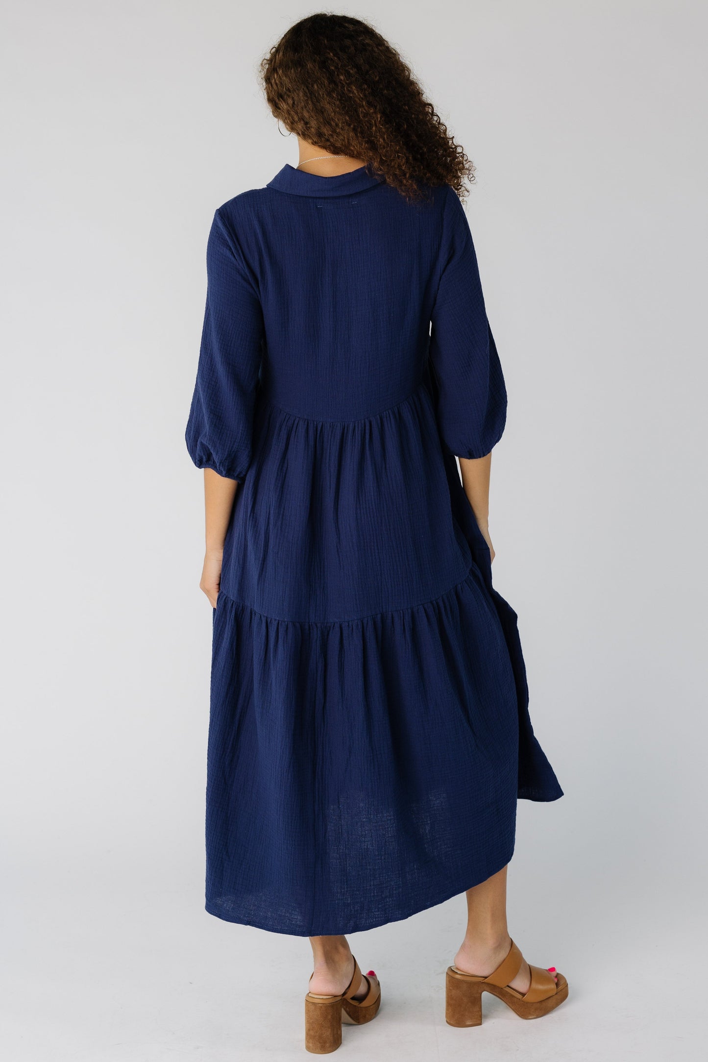Back view of a teen girl wearing a navy tiered midi dress with three quarter sleeves
