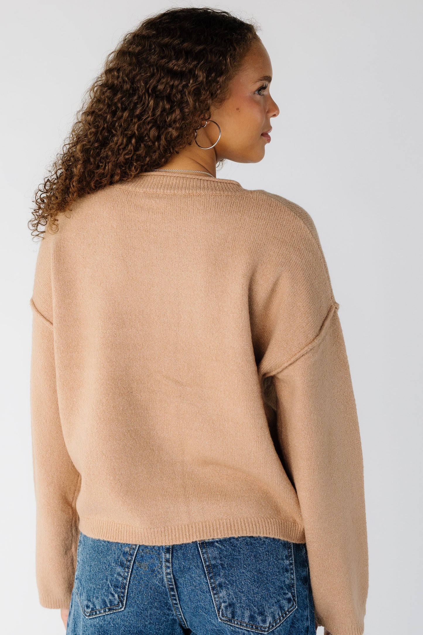 Back view of a woman wearing a taupe long sleeve sweater with drop shoulders and exposed sleeves