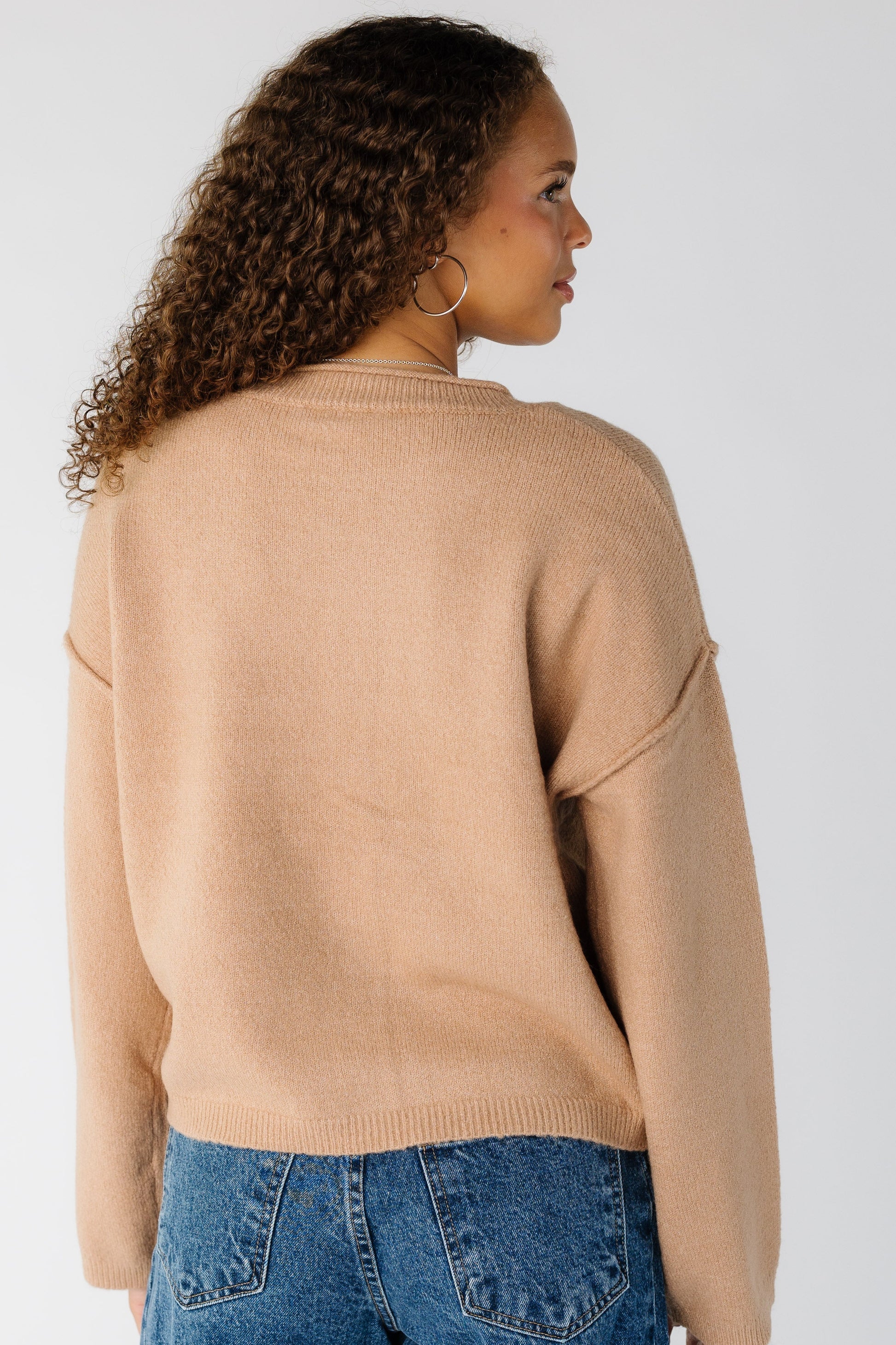 Back view of a woman wearing a taupe long sleeve sweater with drop shoulders and exposed sleeves