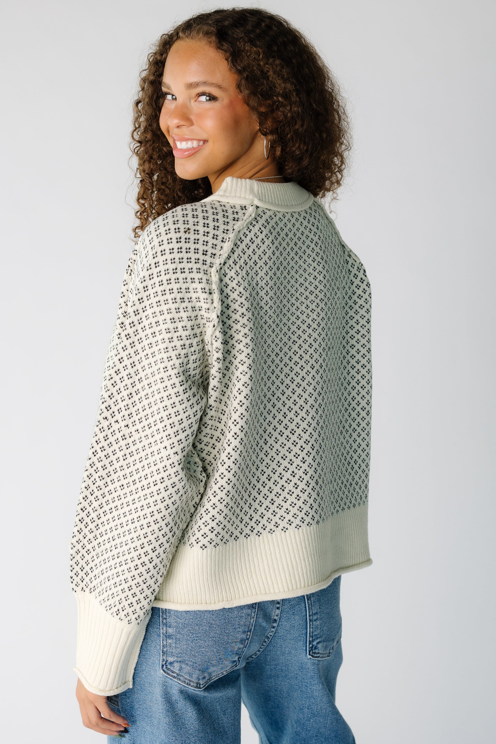 Back view of a teen girl wearing a cream & black patterned pullover sweater with long raglan sleeves