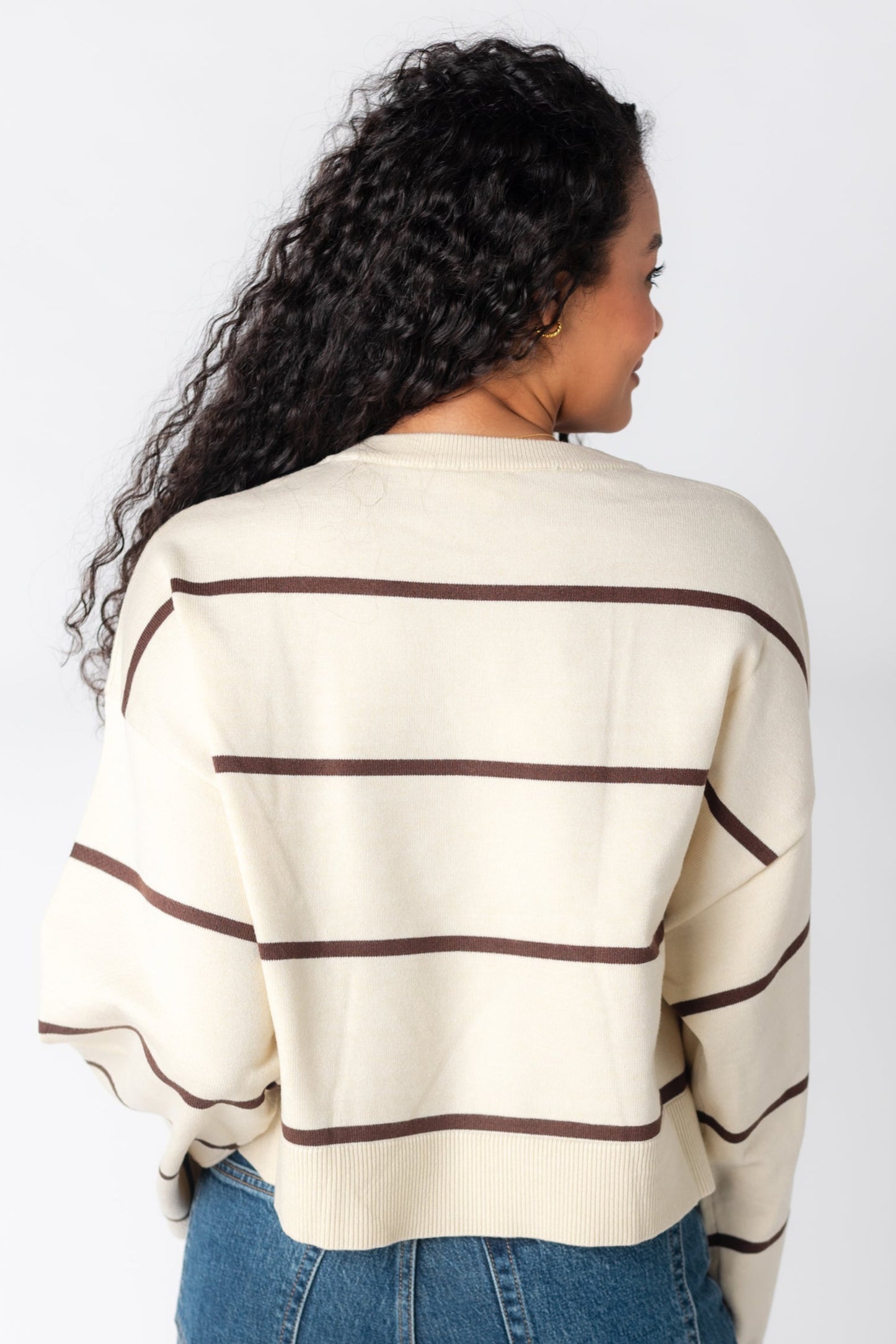 Back view of cream sweater with brown narrow stripes and crew neckline and loose sleeves