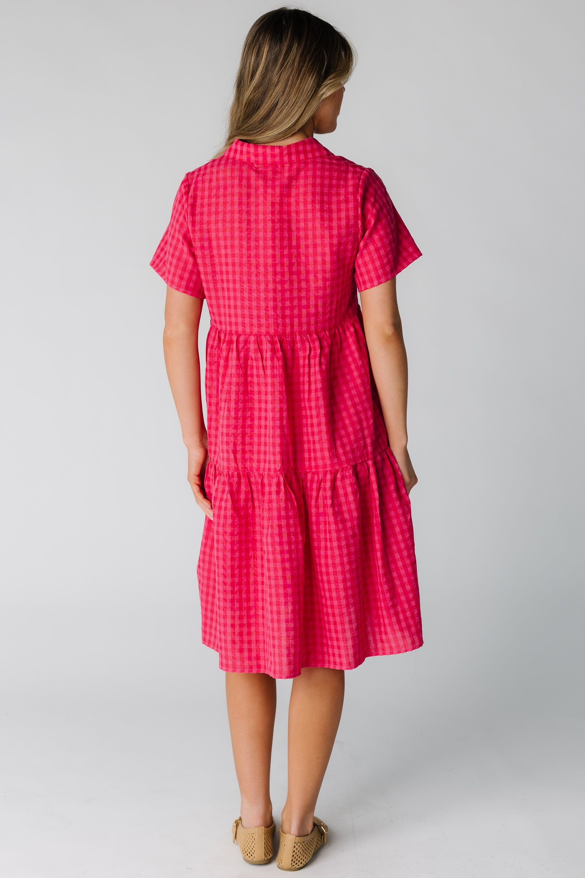 Back view of a woman wearing a loose fitting red gingham dress with short sleeves.