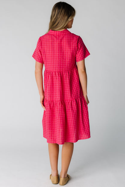 Back view of a woman wearing a loose fitting red gingham dress with short sleeves.