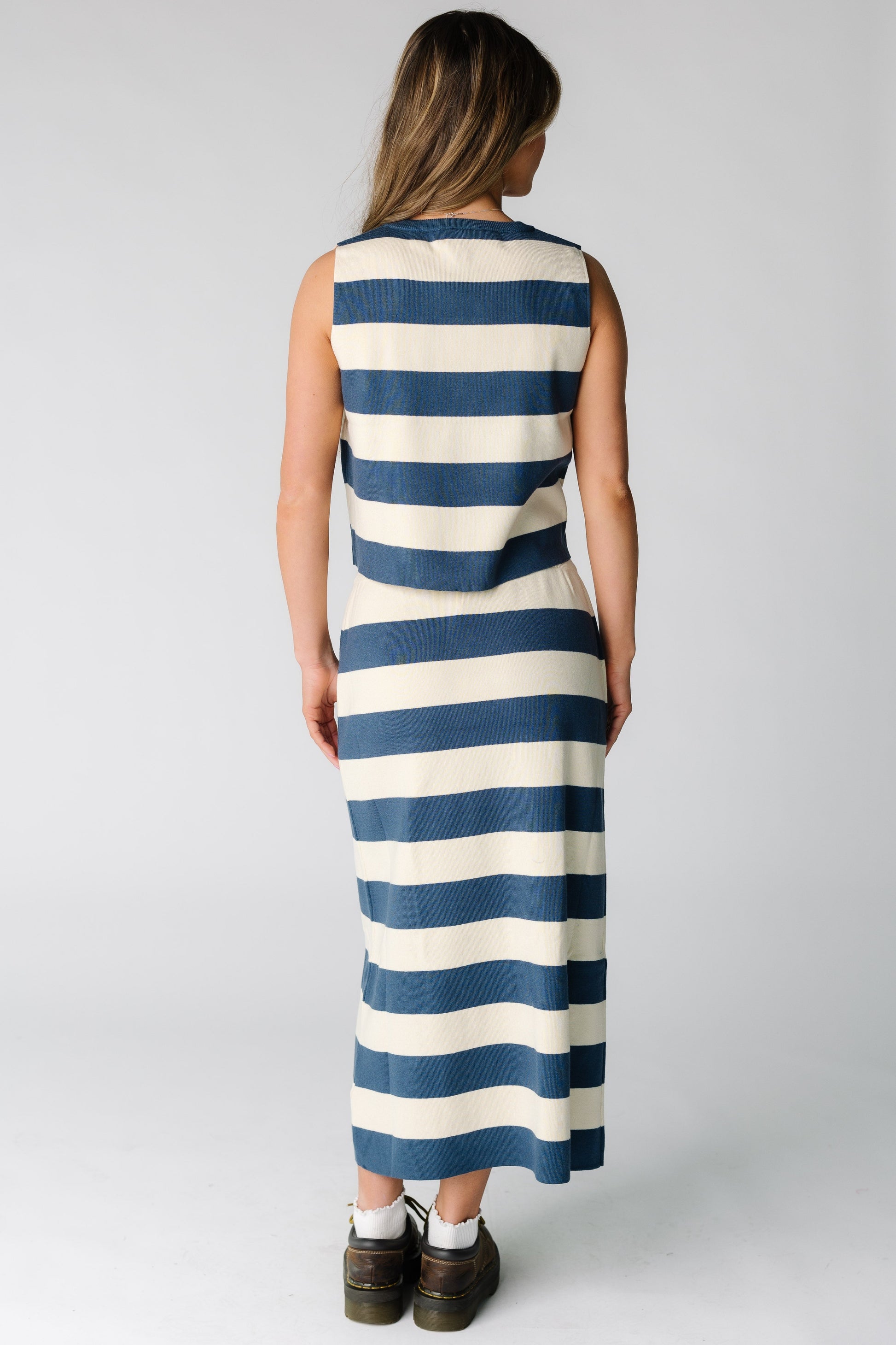 Back view of a woman wearing a blue and cream wide stripe skirt and top set with a midi skirt and sleeveless top.