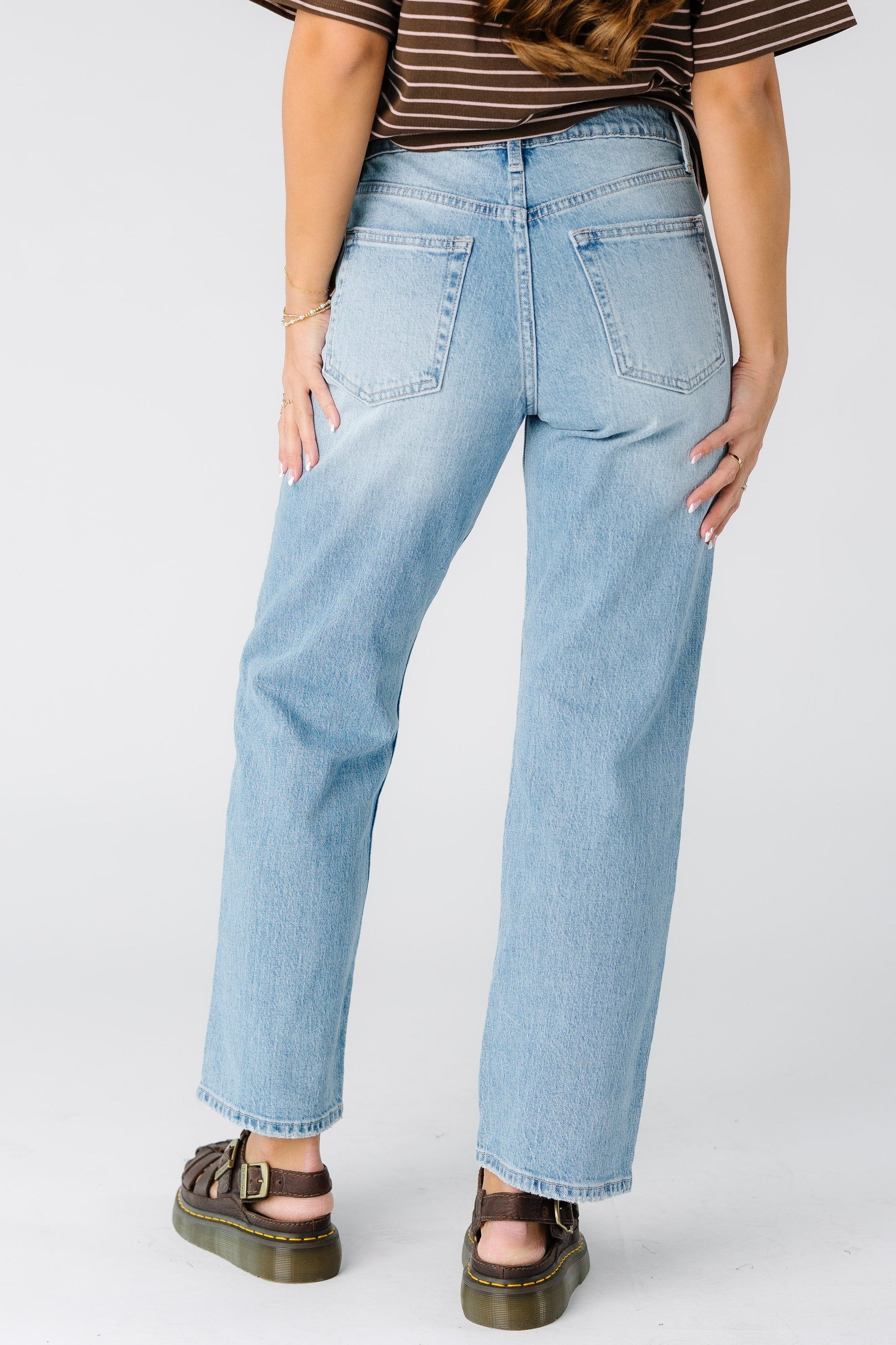 Back view of a woman wearing a pair of  hemmed light denim jeans.