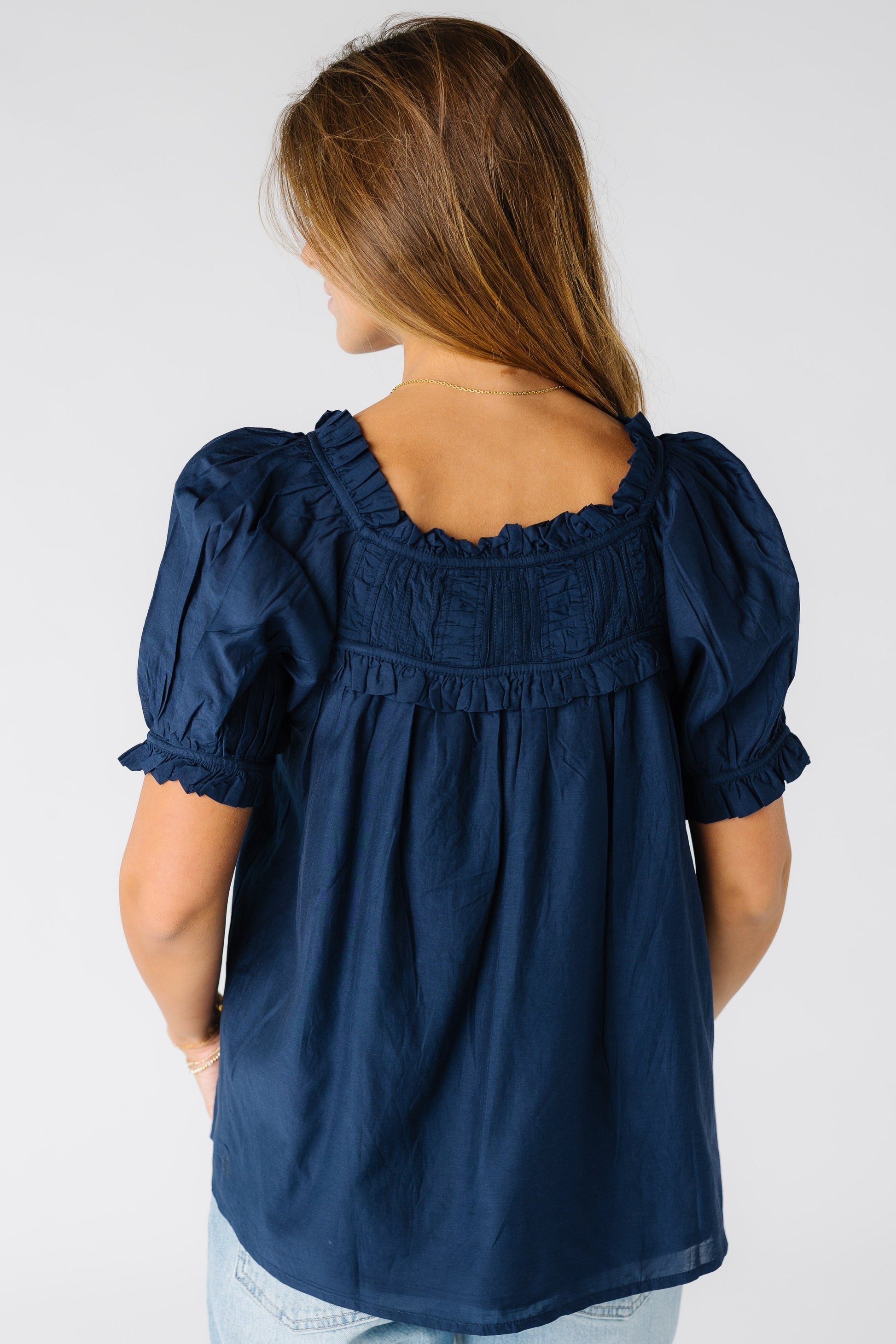 Back view of a woman wearing a loose fitting navy top with a square neckline and short sleeves
