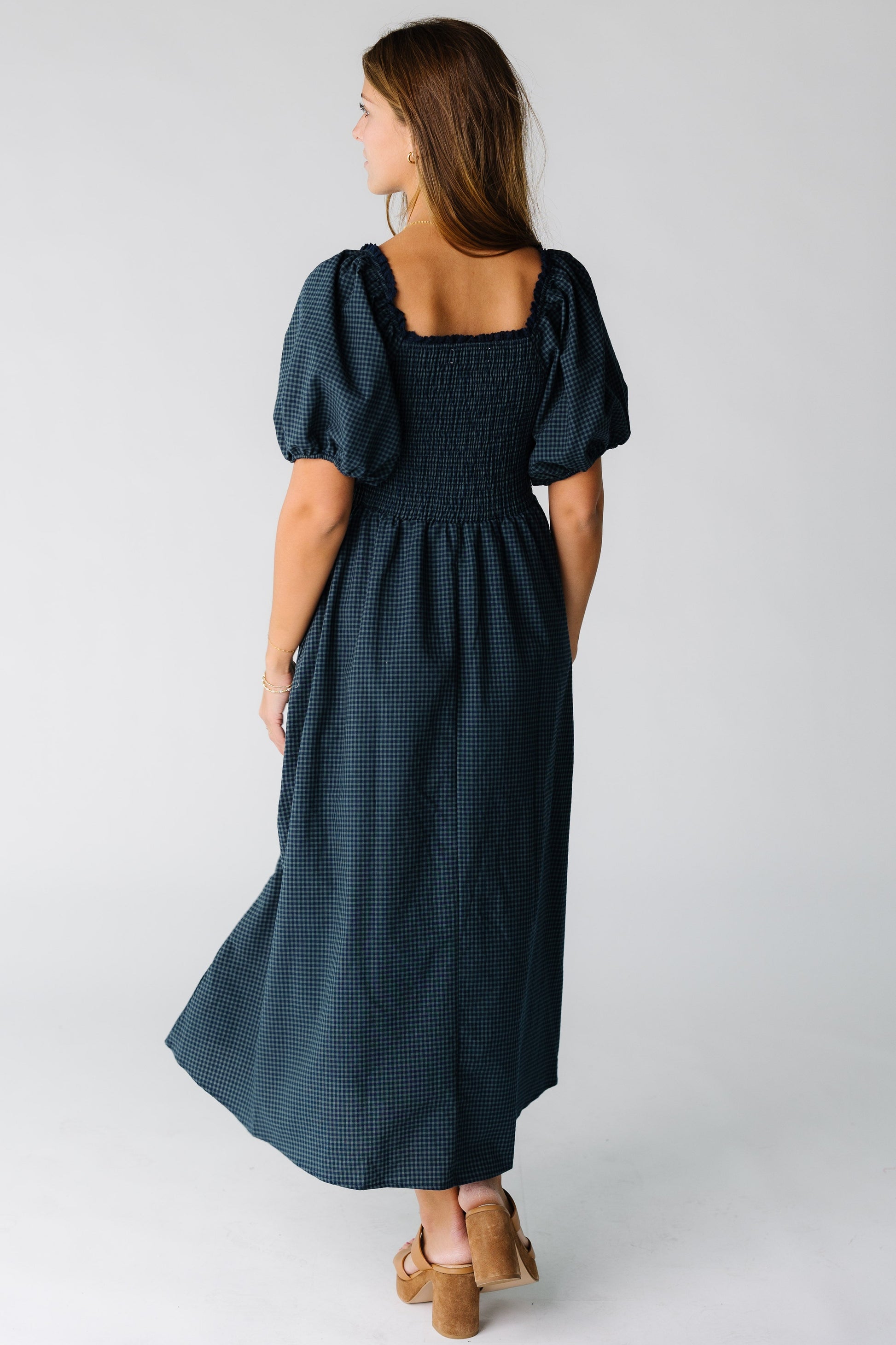Back view of a woman wearing a navy gingham midi dress with short balloon sleeves and square neckline