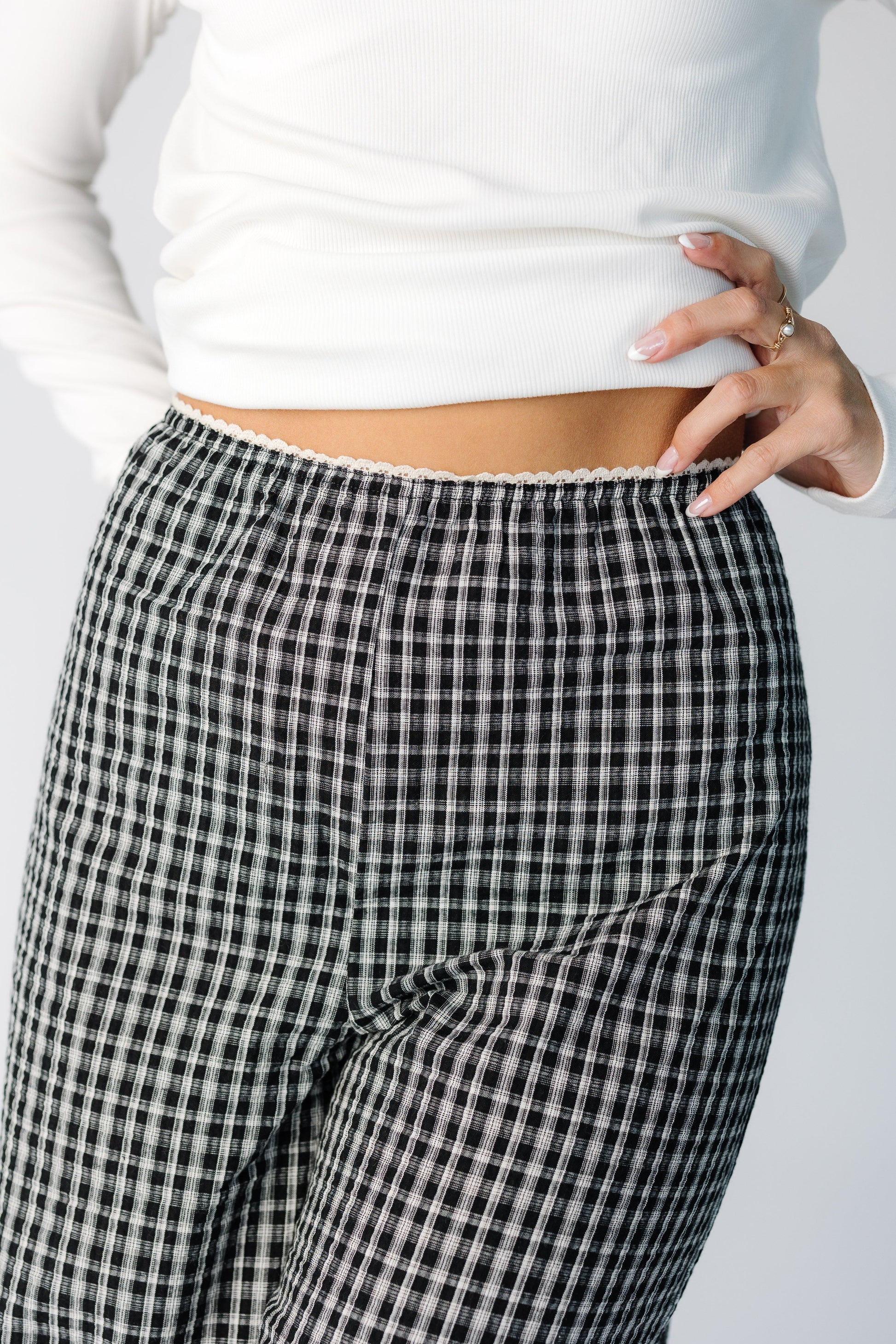 Close view of a woman wearing a pair of black plaid pants with a narrow elastic waist with lace trim