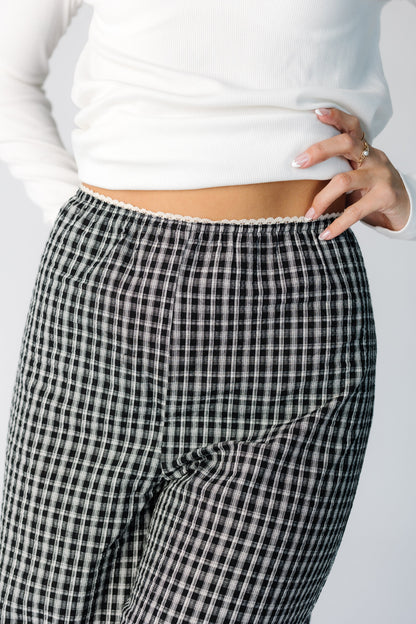 Close view of a woman wearing a pair of black plaid pants with a narrow elastic waist with lace trim